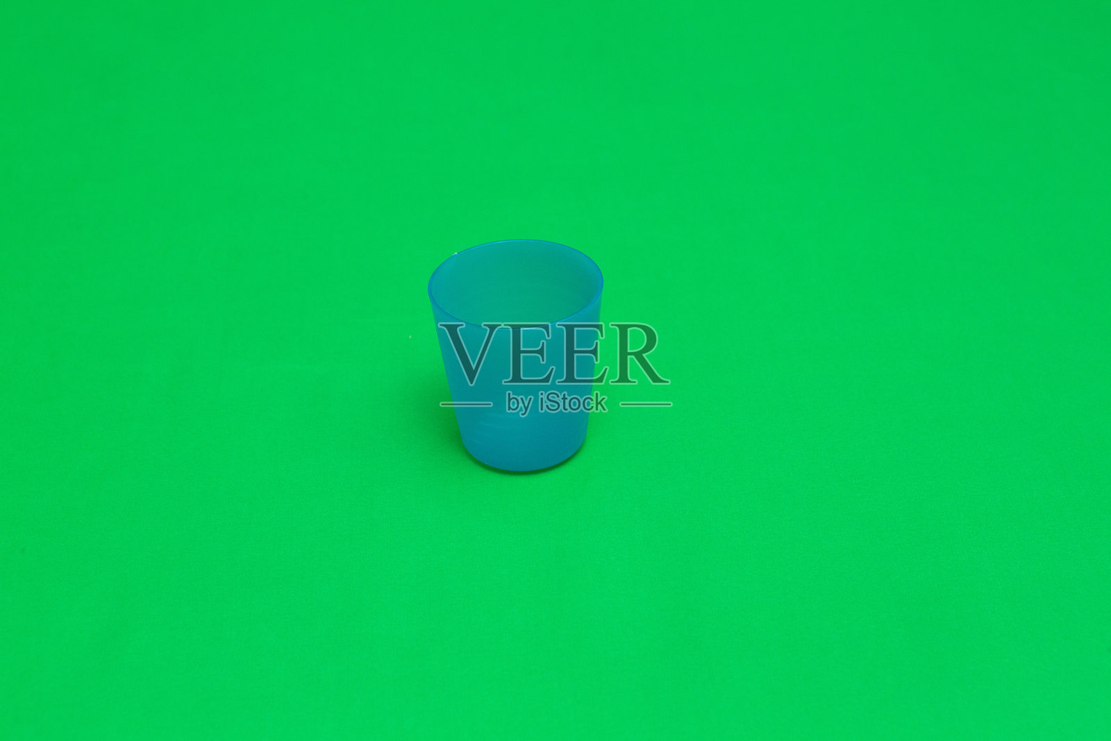 小蓝色塑料杯放在绿色背景上照片摄影图片