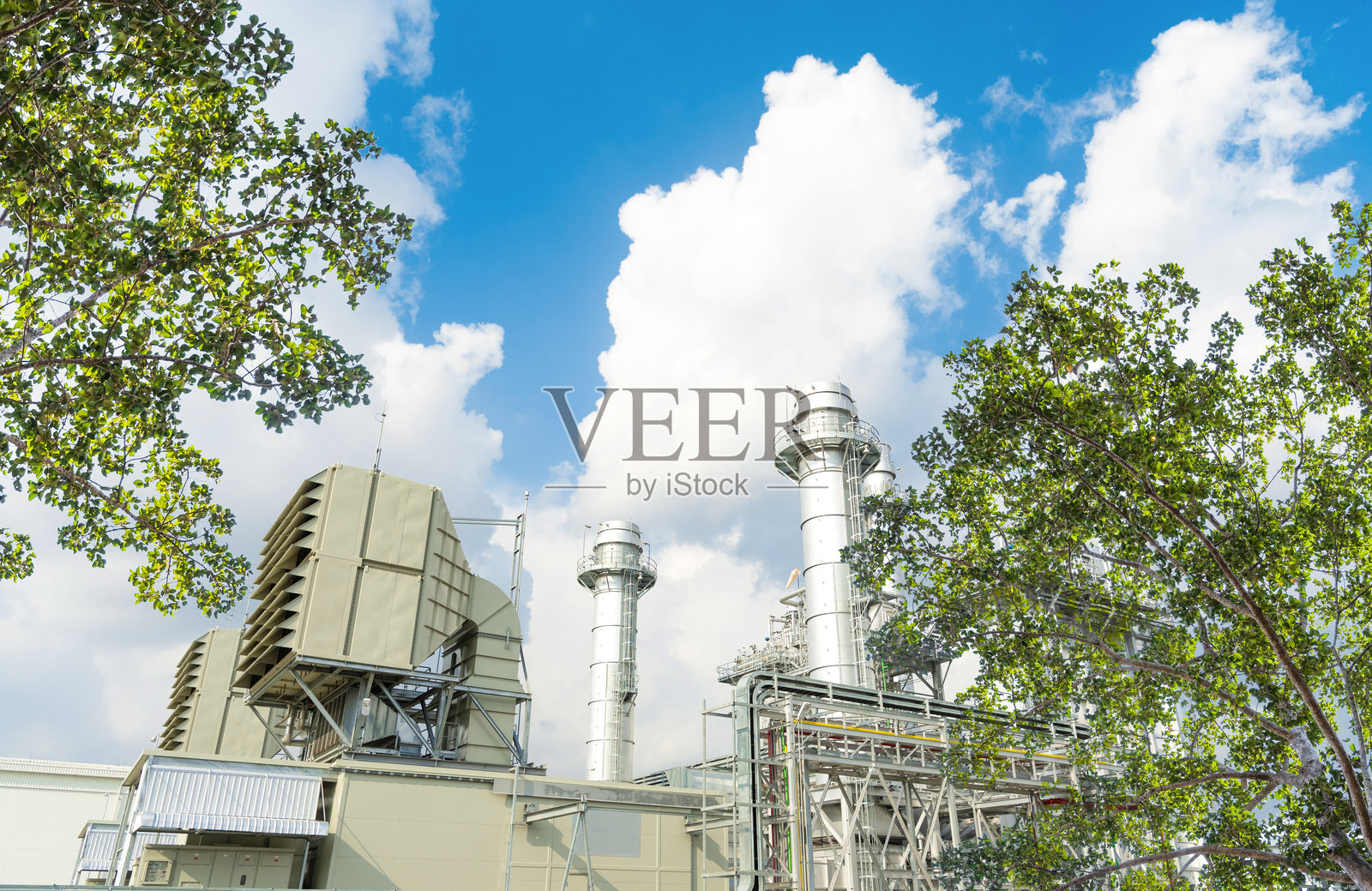 工业区的石油炼油厂,周围有郁郁葱葱的绿树和蓝天。照片摄影图片
