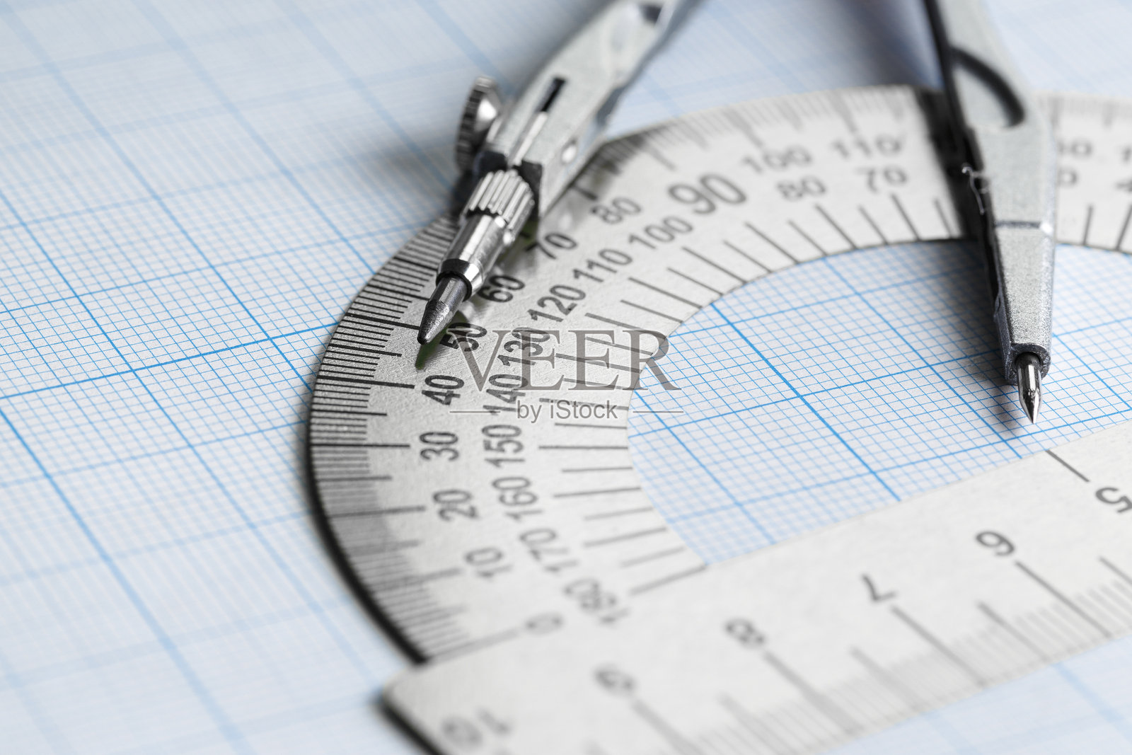蓝色方格纸上的量角器和圆规。照片摄影图片