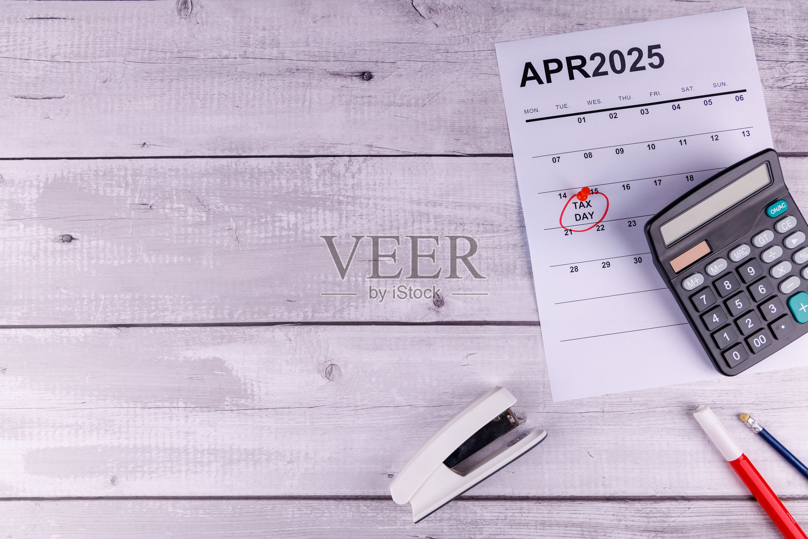 红色圈出的4月15日,旁边有计算器、铅笔和1099税表,放在白色木桌上,象征着报税截止日期。照片摄影图片