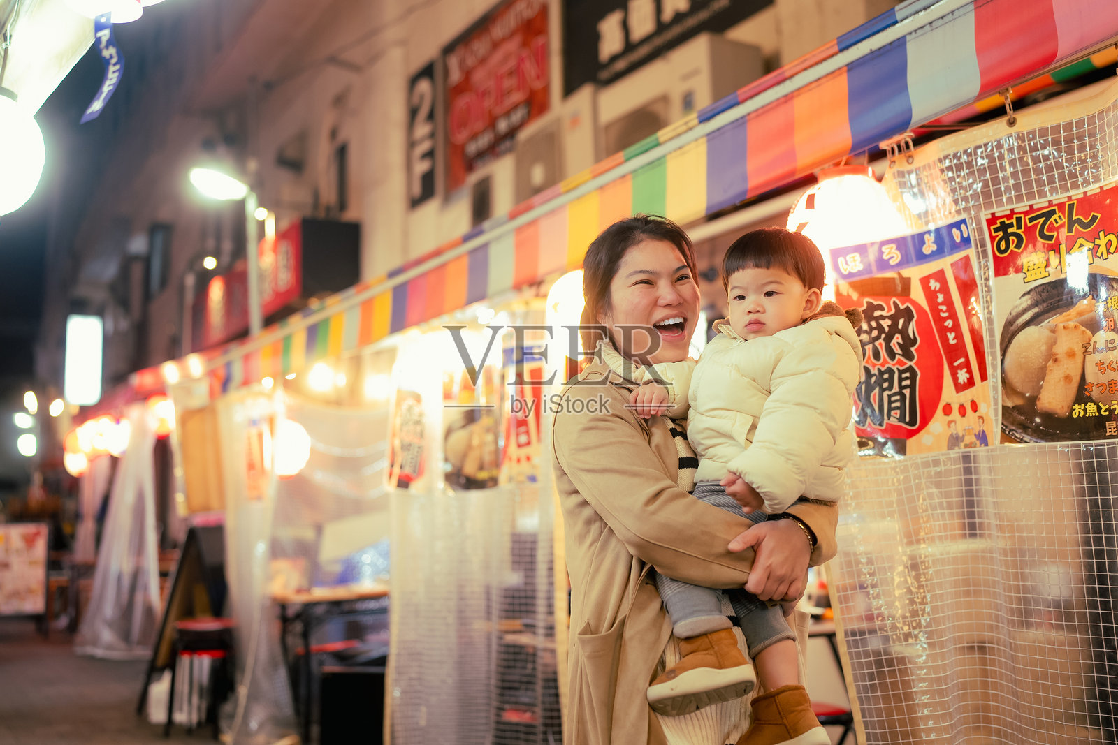 年轻的亚洲母亲在日本的夜晚,拥抱着可爱的小儿子,享受着美丽的城市街道生活。照片摄影图片