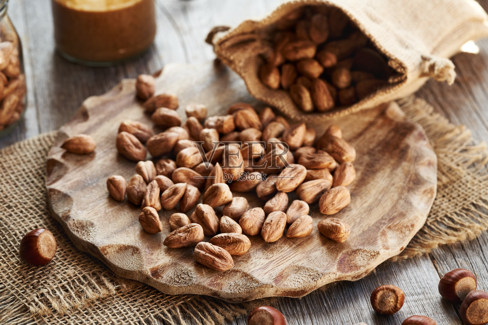 从麻袋中洒出的去壳榛子,背景中有一瓶坚果酱照片摄影图片