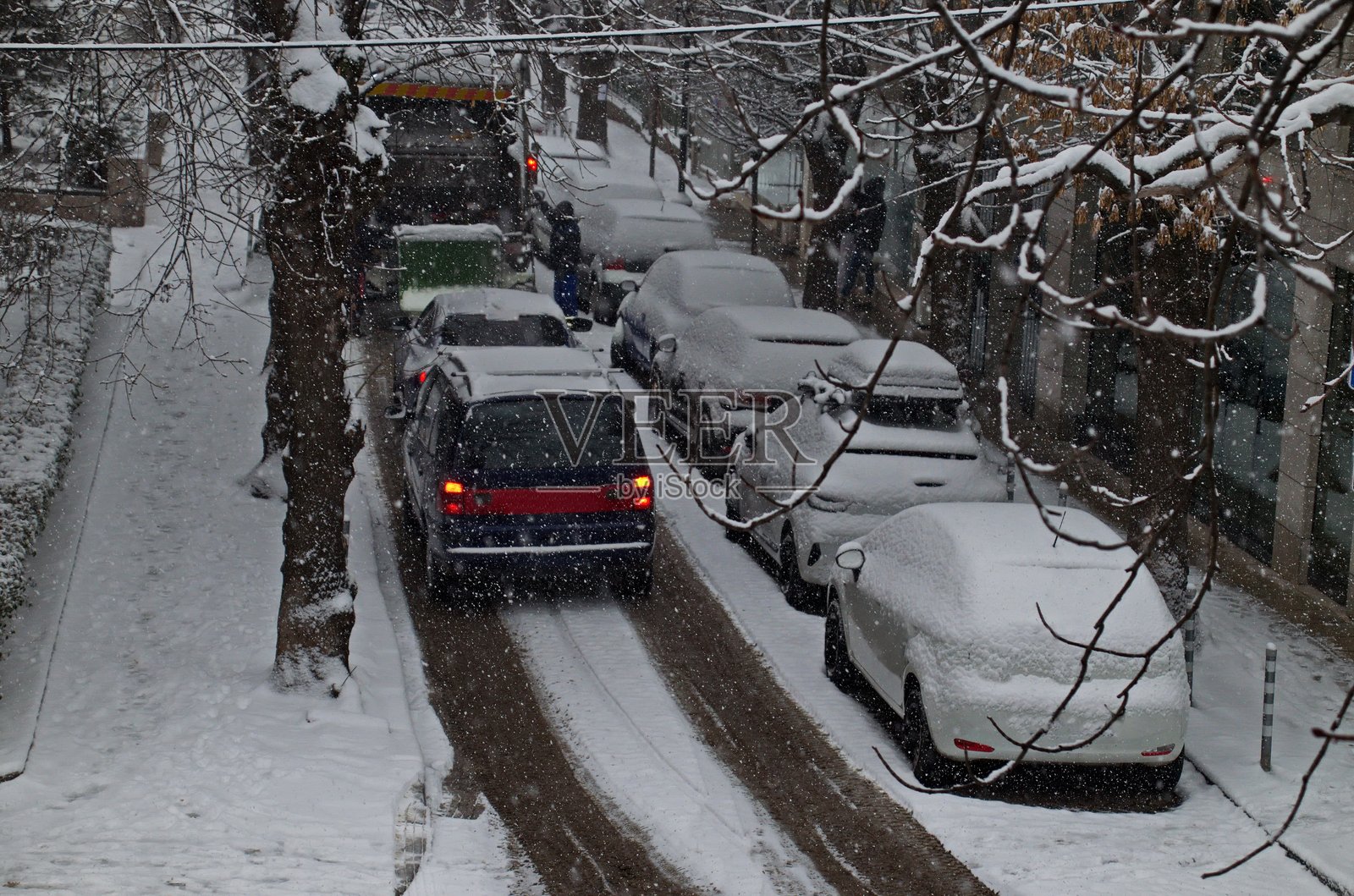 暴风雪中强风肆虐,狭窄街道上停着汽车和一辆垃圾车,索非亚。照片摄影图片
