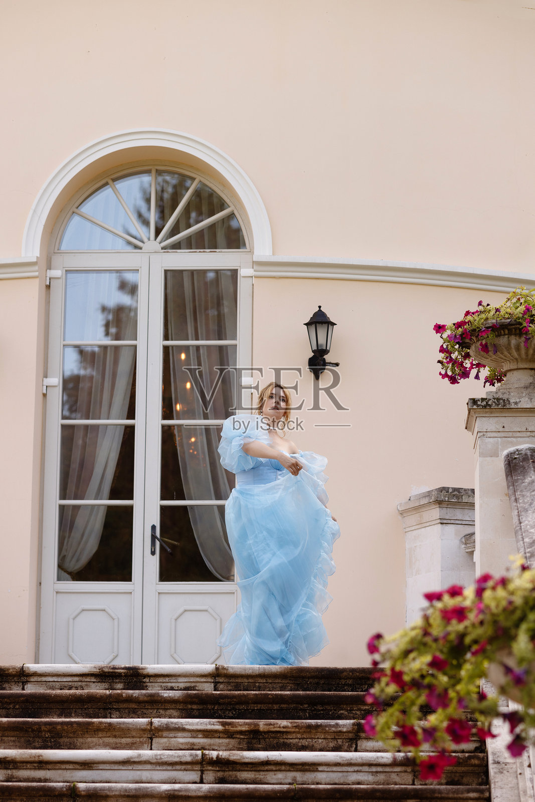 优雅的女性穿着流动的蓝色长裙走下古老的石阶照片摄影图片