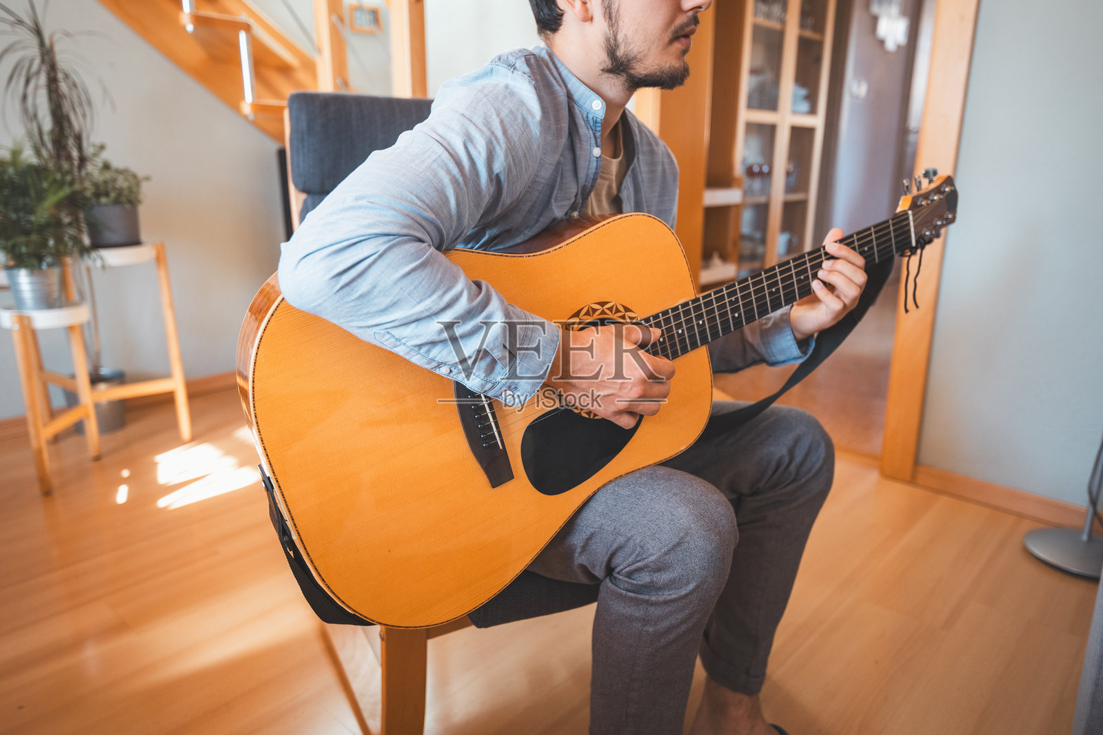 一个人独自在阳光明媚的房间里,享受着弹奏美丽的木制原声吉他并创作新歌曲。沉浸在吉他的甜美音色中。音乐治愈心灵。照片摄影图片