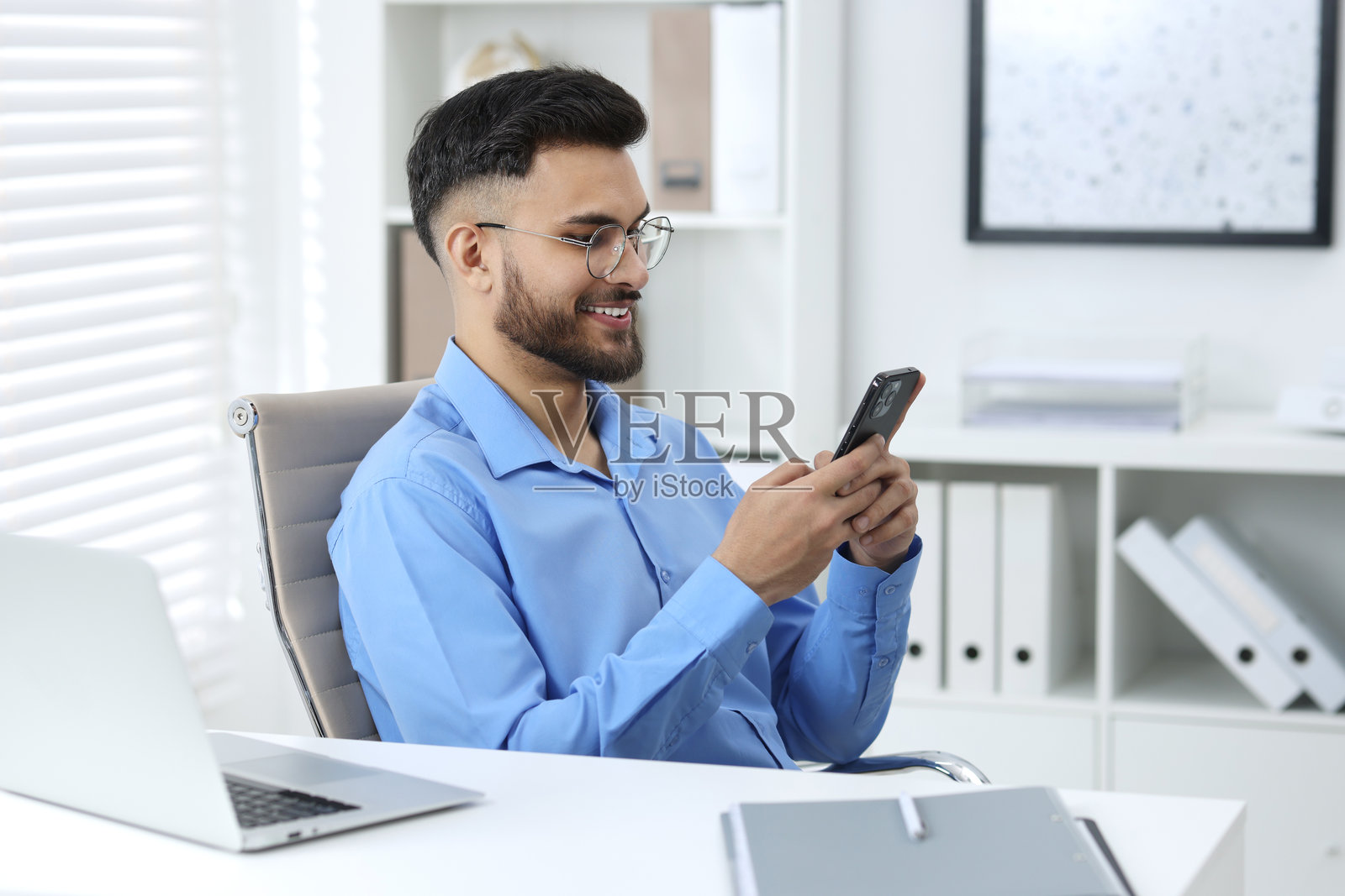 快乐的年轻人在办公室的白色桌子上使用智能手机照片摄影图片