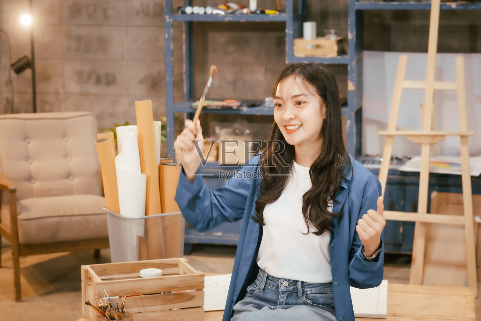 一位快乐的亚洲少女在家中用画笔在画布上作画,享受创造力和放松的时光,周围是充满艺术灵感和鲜艳色彩的舒适宁静环境。照片摄影图片