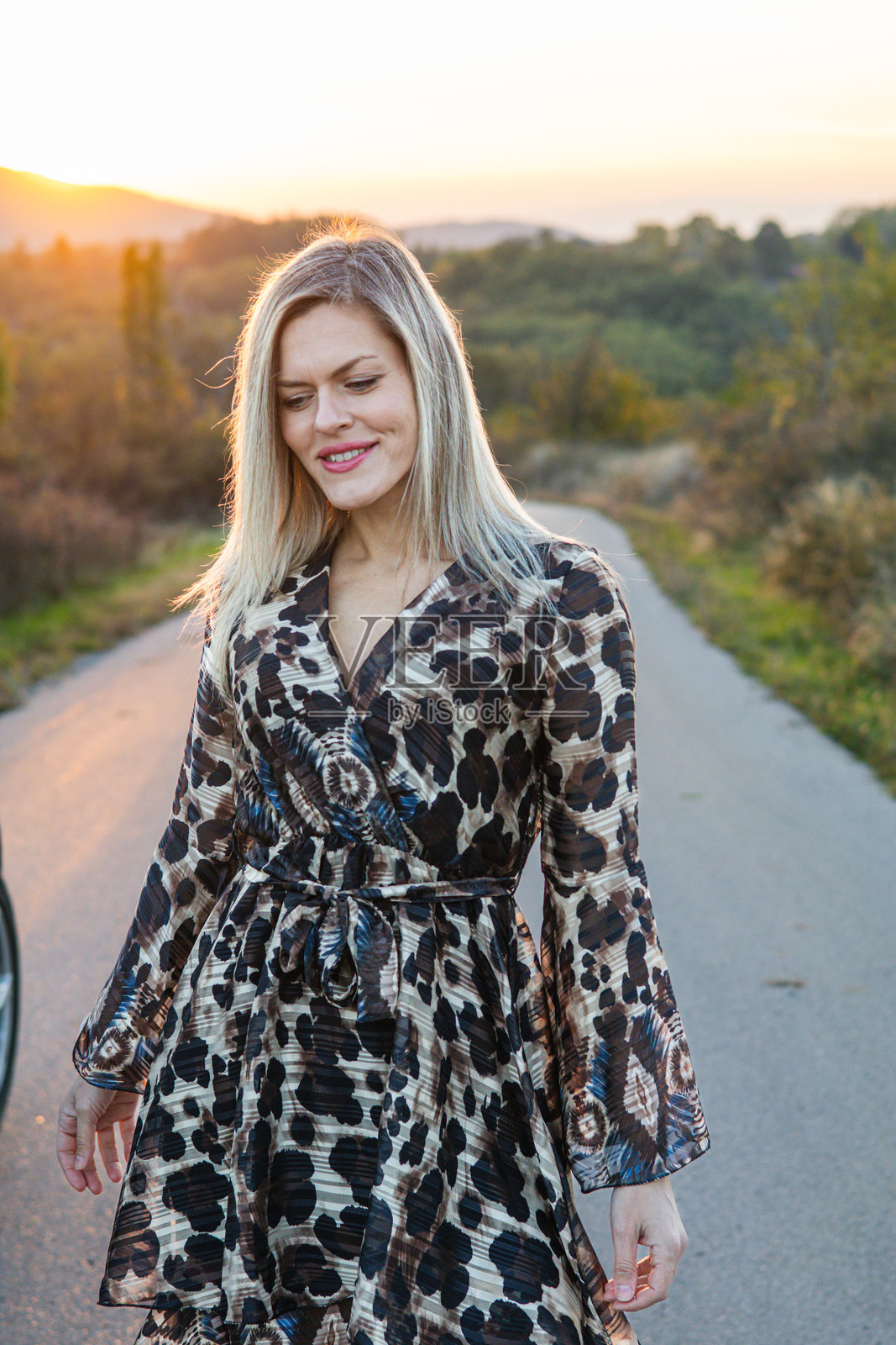 穿着裙子的金发女人在开车时休息。她正在享受日落,欣赏风景。自由的概念。照片摄影图片