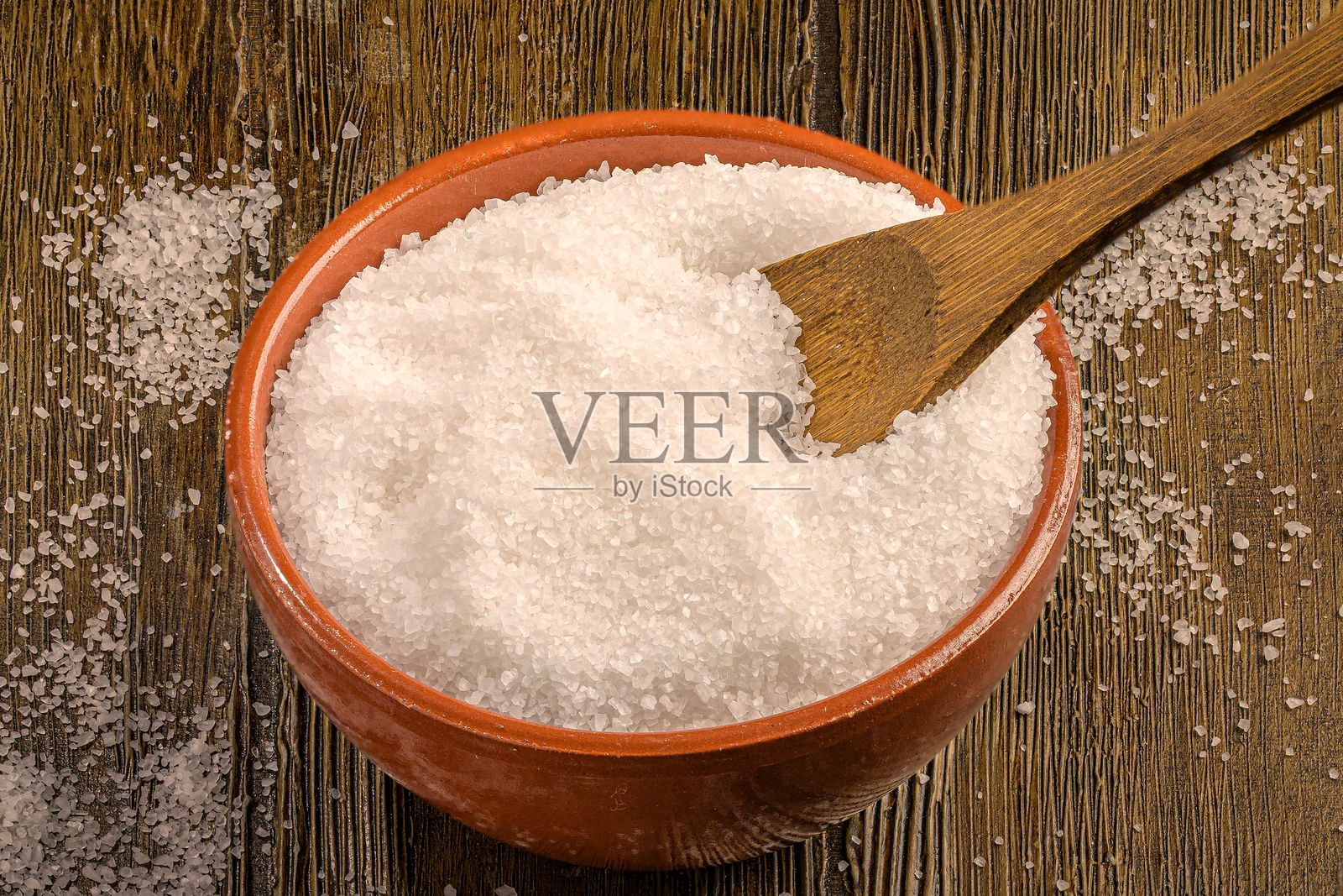 粗海盐放在陶土碗中,旁边有一把木勺。照片摄影图片