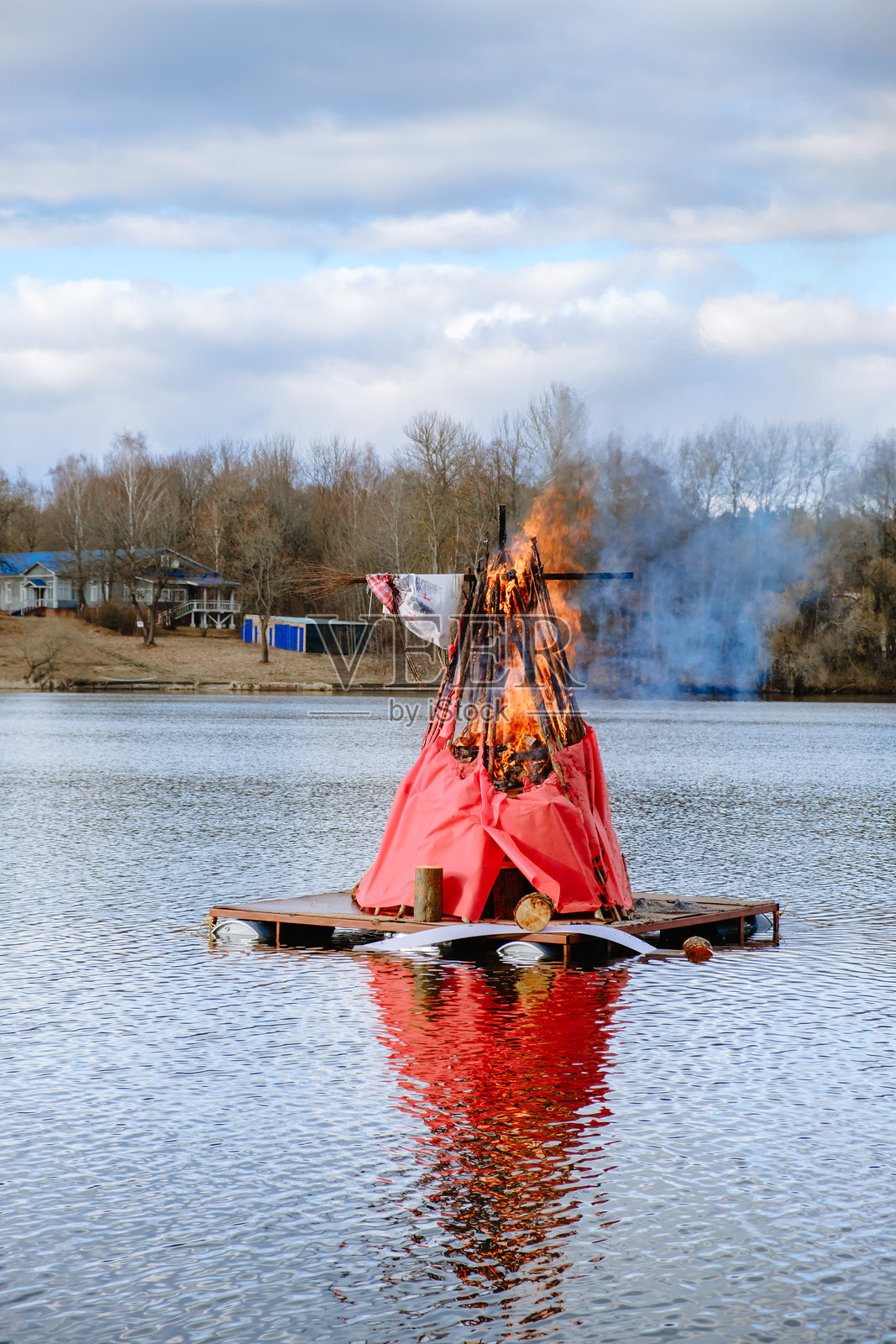 在河边焚烧马斯连尼察的稻草人。火焰中的玩偶。谢肉节庆祝活动是一个传统的斯拉夫节日,象征着春天的到来。焚烧稻草人的仪式象征着冬天的结束。照片摄影图片