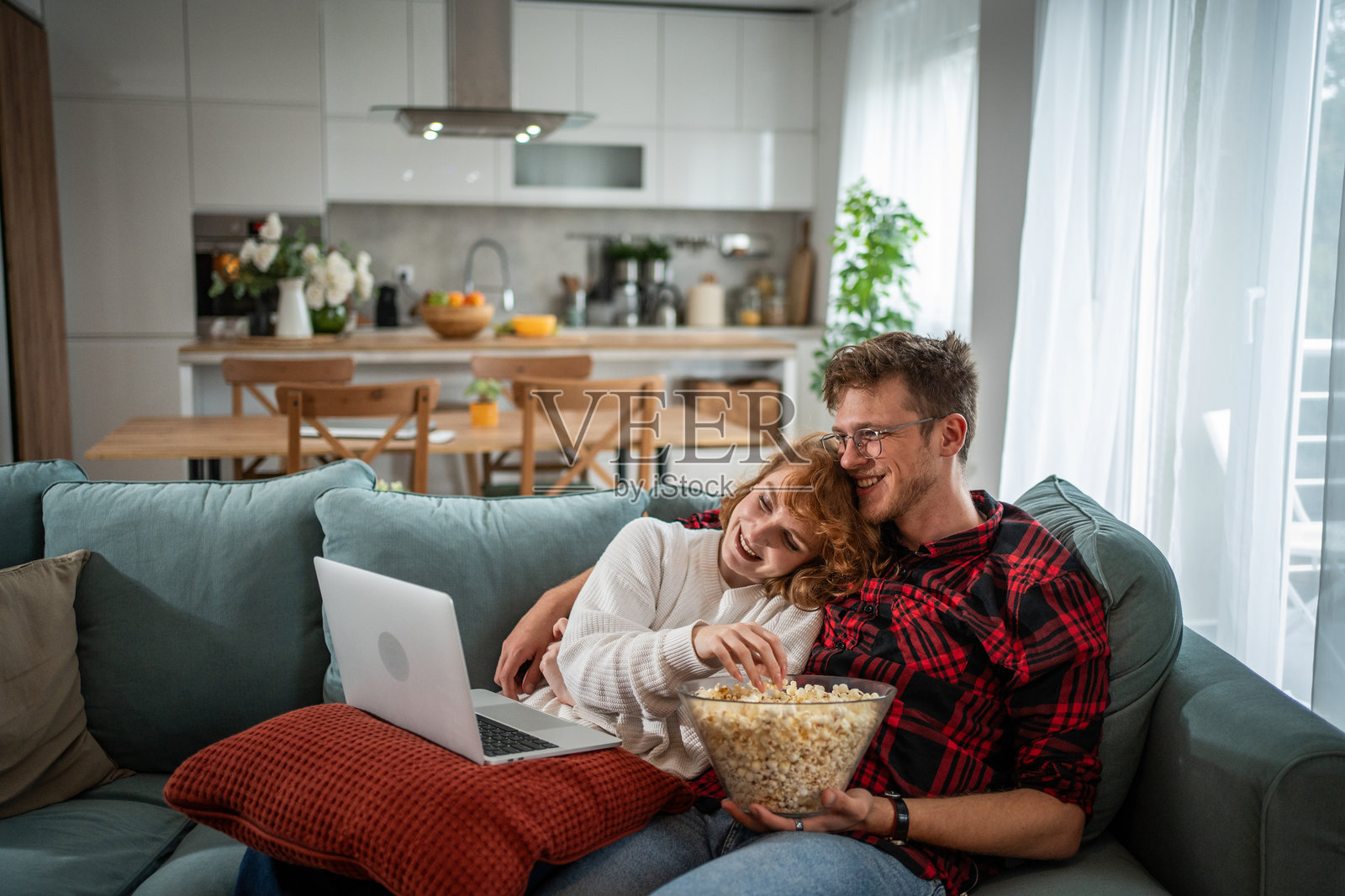 年轻情侣在家沙发上看笔记本电脑电影,吃着爆米花照片摄影图片