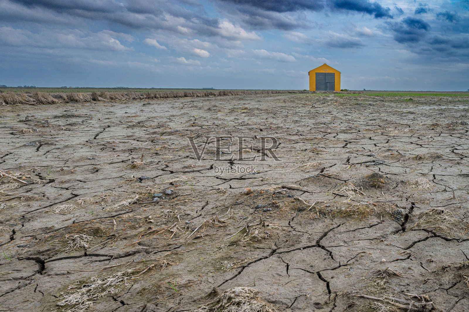 干旱裂缝的干稻田和孤独的黄色建筑在阴云密布的天空下照片摄影图片