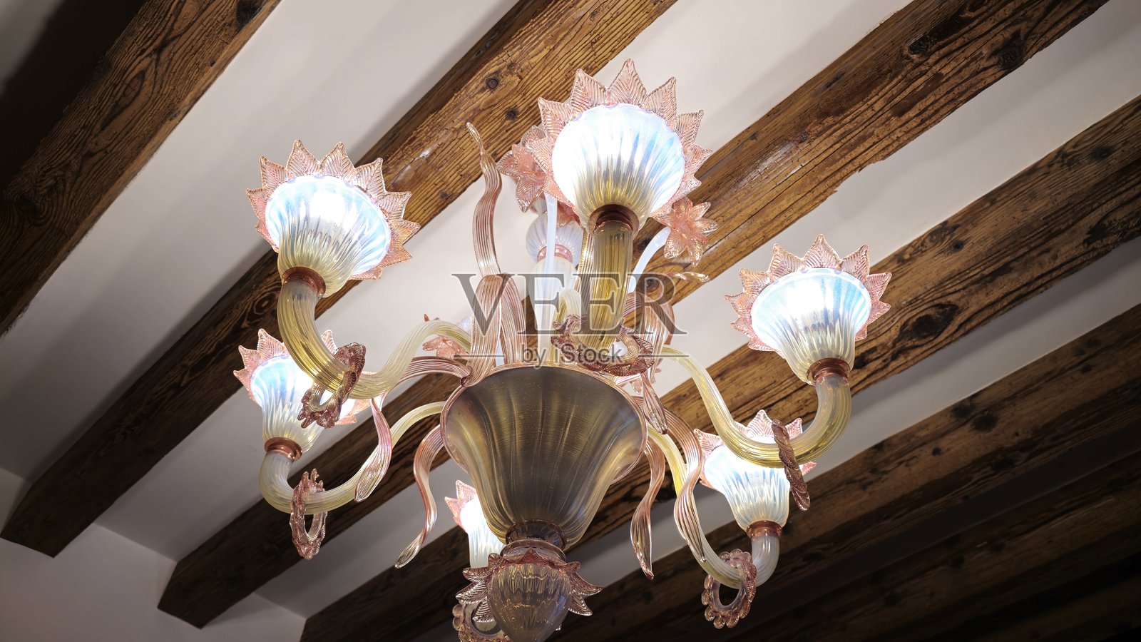 一盏优雅的穆拉诺玻璃吊灯,带有精致的花卉设计,柔和地照亮着带有木梁的乡村天花板,展现出威尼斯工艺与历史魅力的完美结合。照片摄影图片