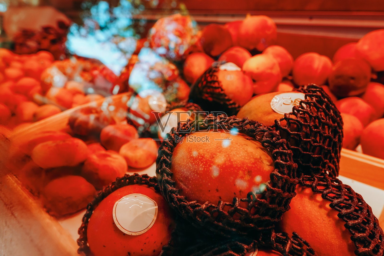 市场上新鲜芒果用保护网包裹,成熟的桃子。温暖的灯光增强了丰富而鲜艳的色彩。照片摄影图片