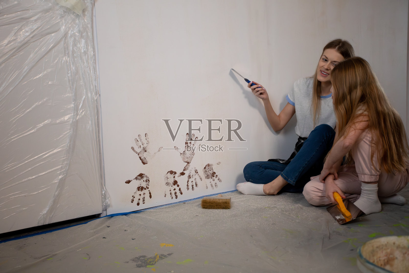 两个女孩在享受创意家居装修体验,正在为一面色彩斑斓的墙壁涂漆照片摄影图片