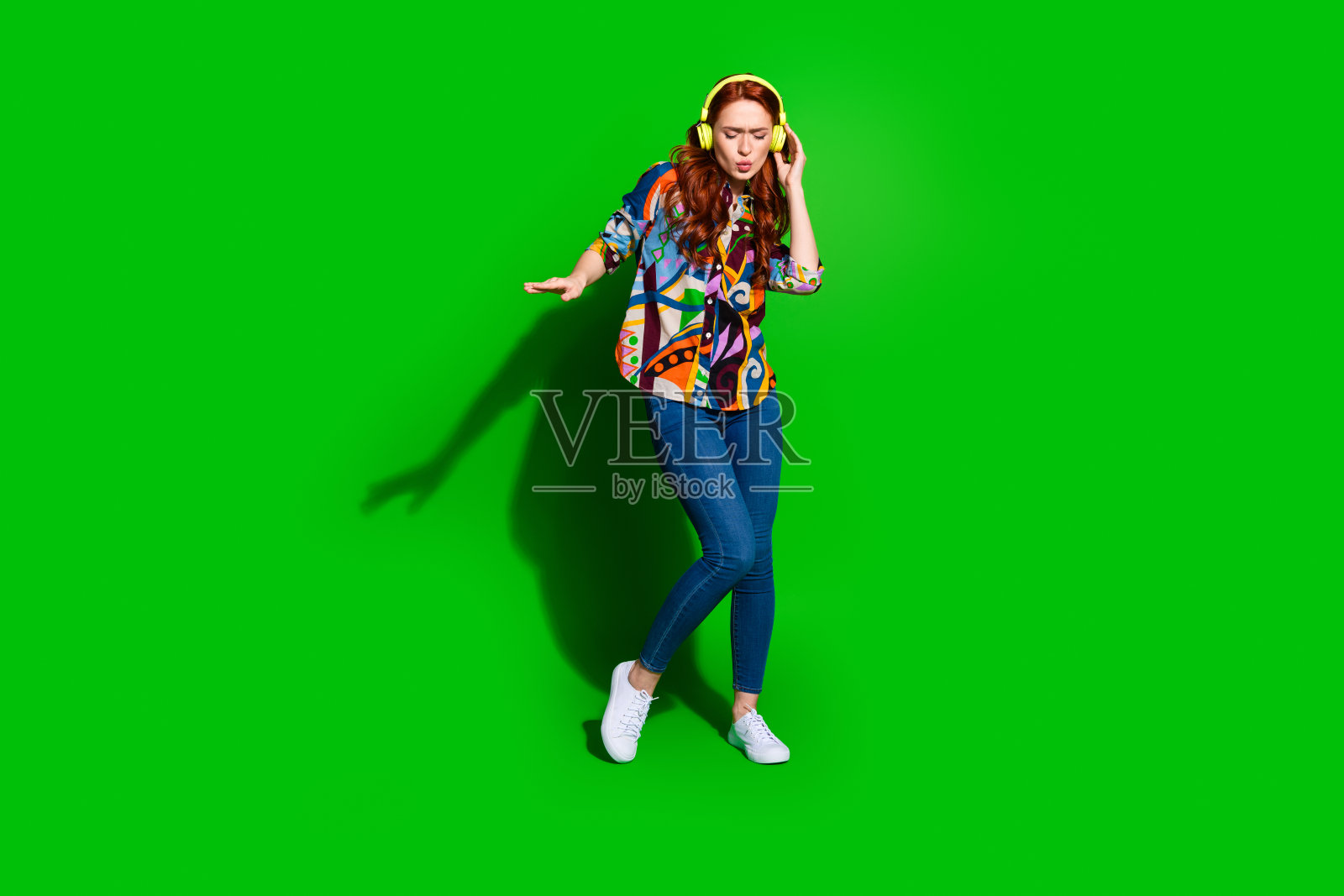 充满活力的年轻女性穿着时尚服装,在生动的绿色背景下享受音乐照片摄影图片