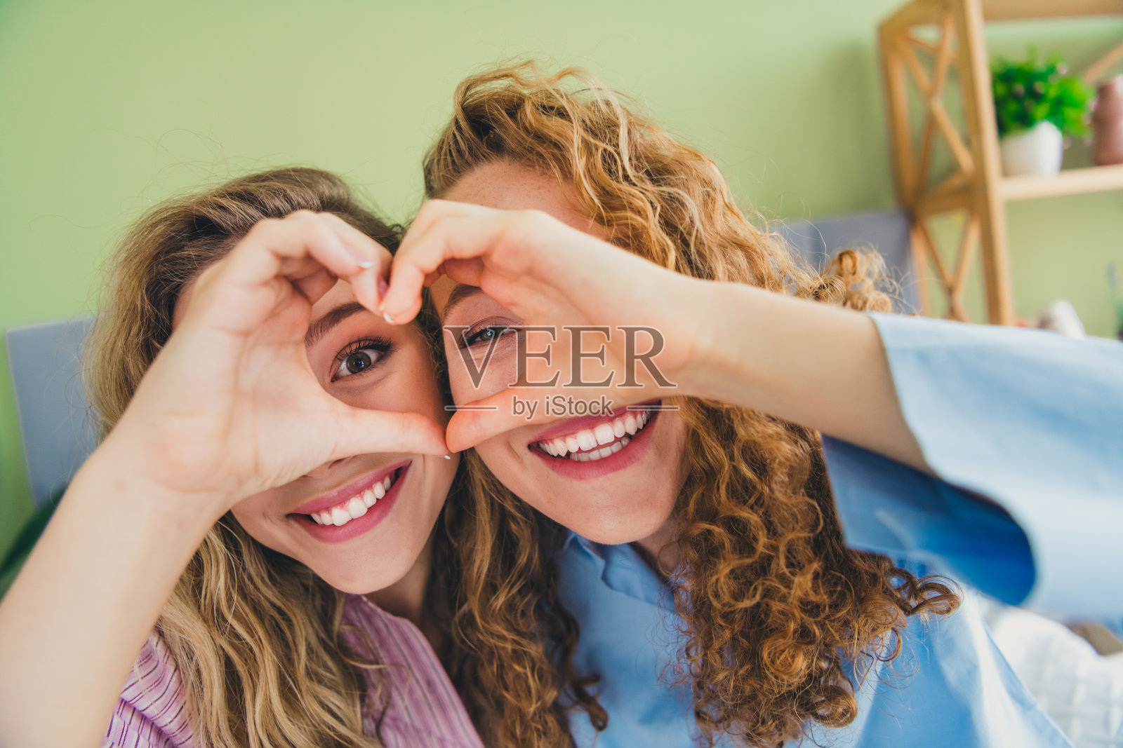 两位可爱的小女孩在现代舒适明亮的卧室里穿着睡衣,做出心形手势,享受刚醒来的时光。照片摄影图片