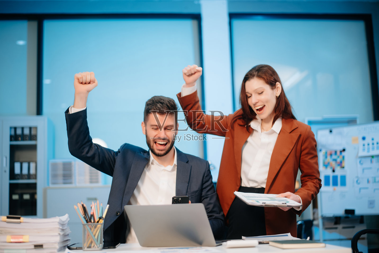 两位办公室同事在现代工作空间中讨论创业项目的想法,使用着笔记本电脑和智能手机。照片摄影图片