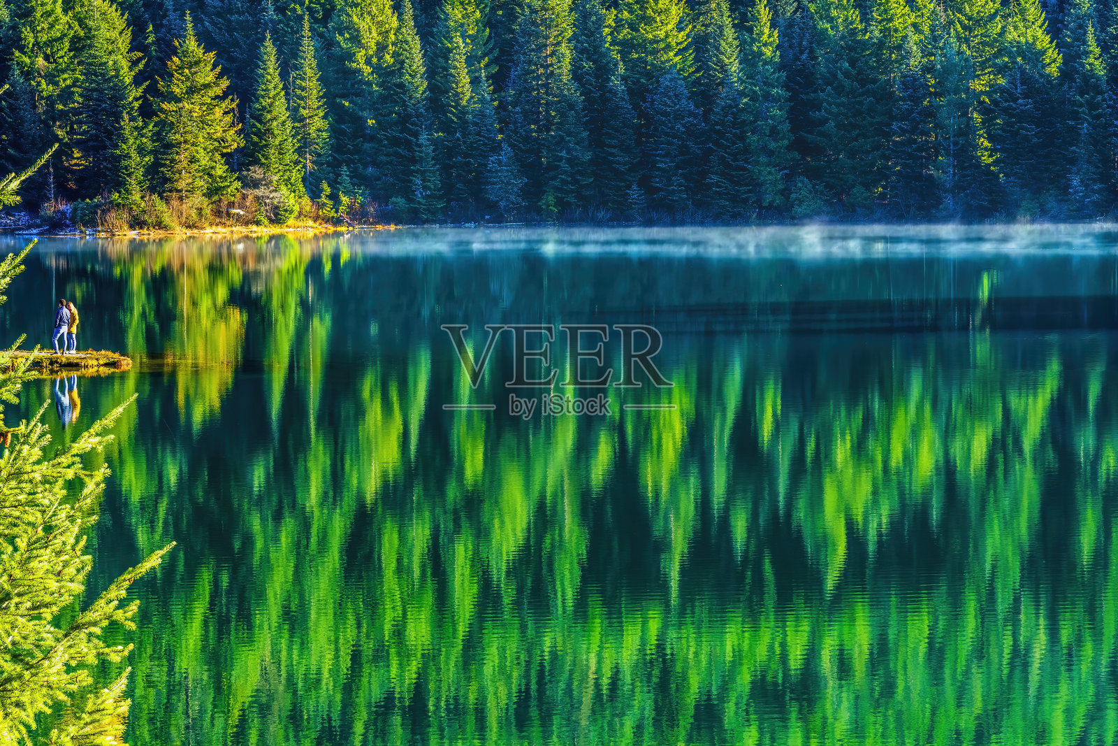 五彩斑斓的徒步旅行者与绿色树木在华盛顿斯诺夸尔米山口的金色湖泊倒影中照片摄影图片