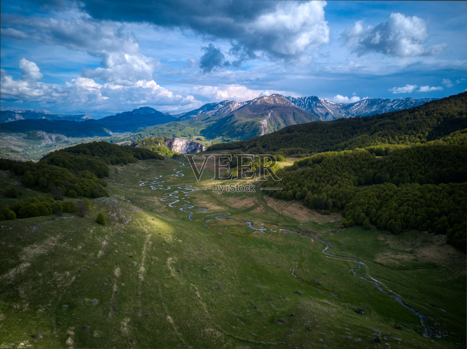风景如画的山谷,蜿蜒的河流、森林和白雪皑皑的山峰在多云的天空下。照片摄影图片
