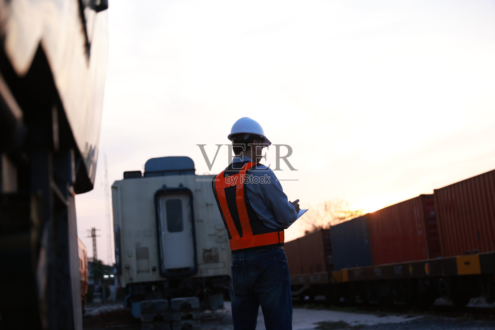 中东男性工程师铁路工人穿着安全帽和安全背心,在货运列车附近的车站检查集装箱货物并使用对讲机工作。照片摄影图片
