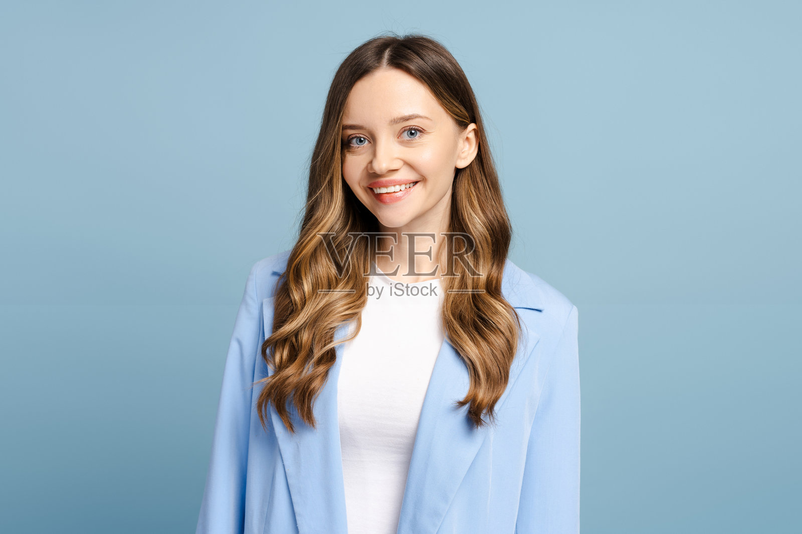 微笑的女商人穿着蓝色夹克,站在浅蓝色背景前摆姿势照片摄影图片