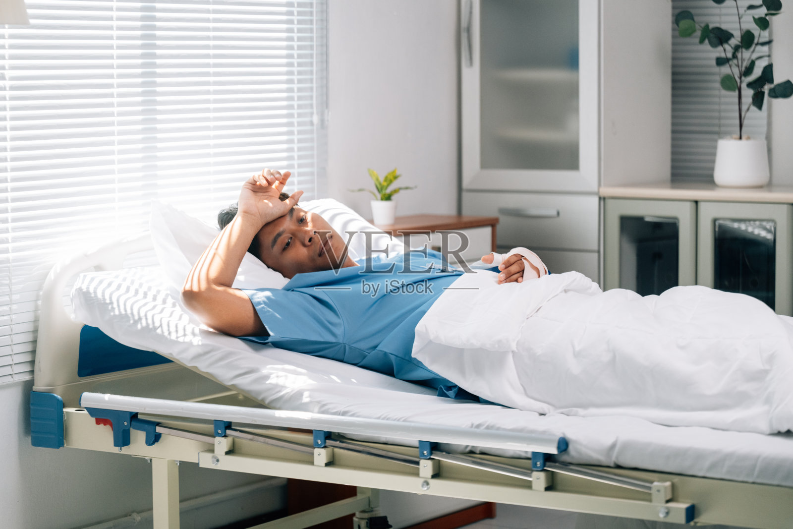 年轻男性患者躺在医院病床上,包扎的手臂静静放着,面露痛苦和痛苦的神情。照片摄影图片