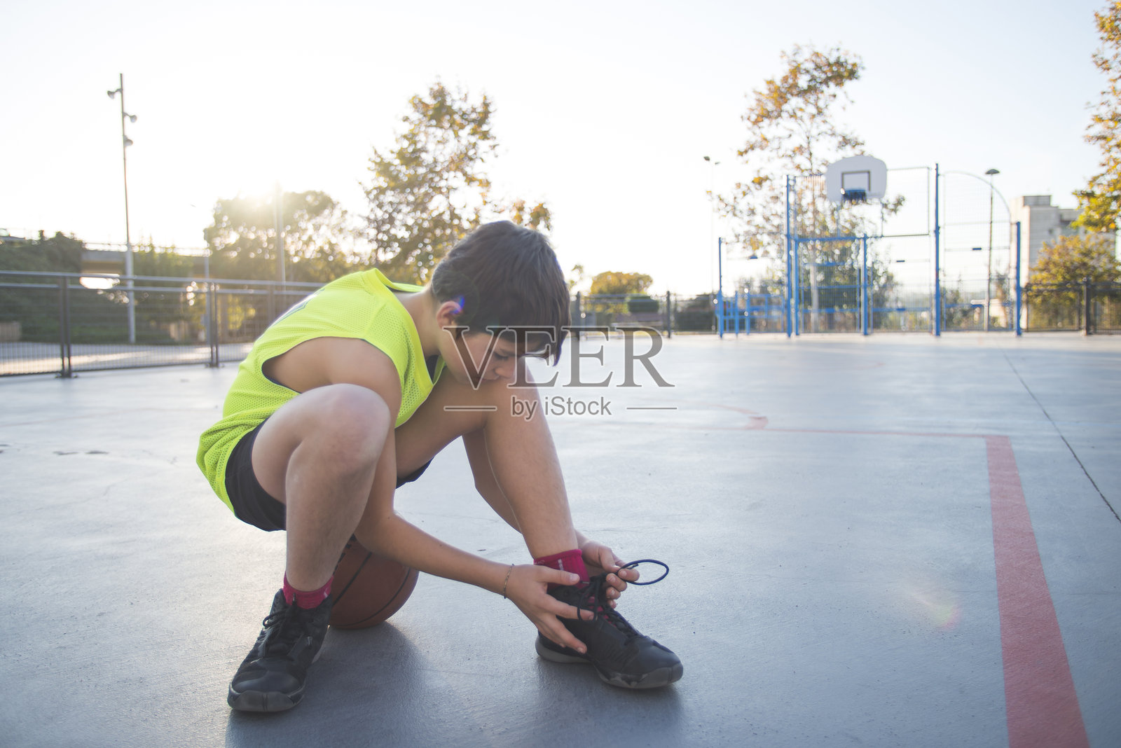 男孩在日落时分的户外篮球场上系鞋带。照片摄影图片
