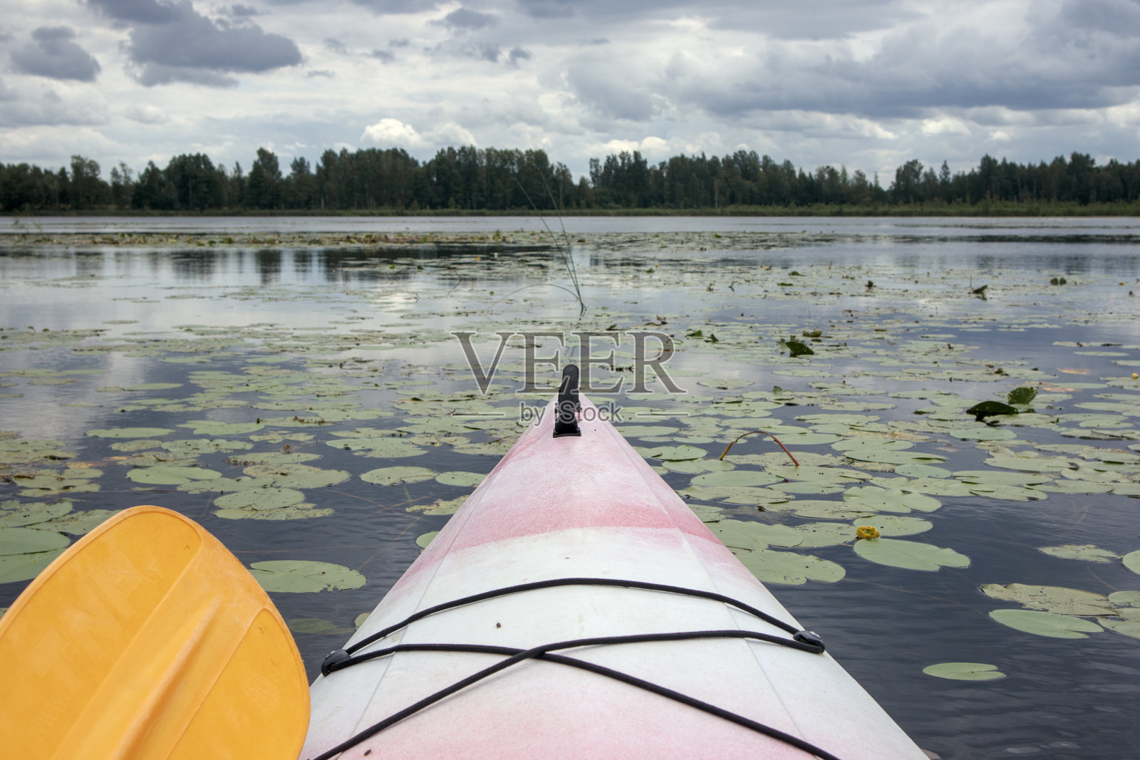 一只皮划艇在河流中漂浮,背景是森林和多云的天空。照片摄影图片