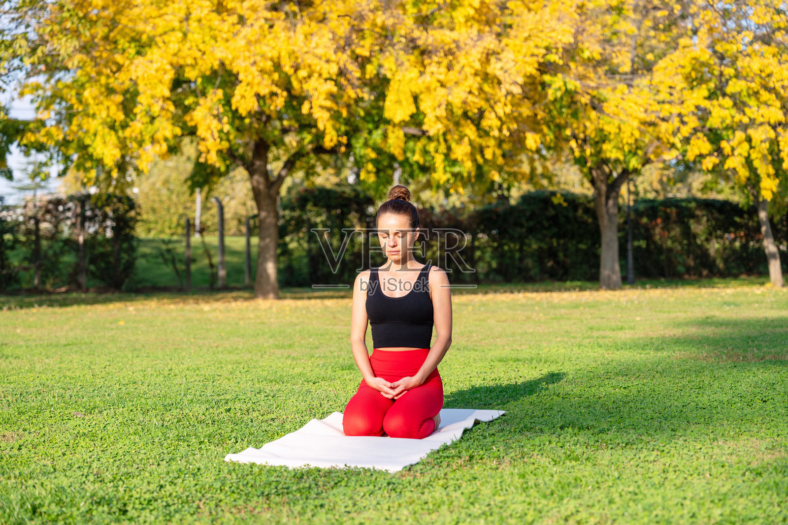 年轻女性在城市公园的阳光明媚的日子里冥想。照片摄影图片