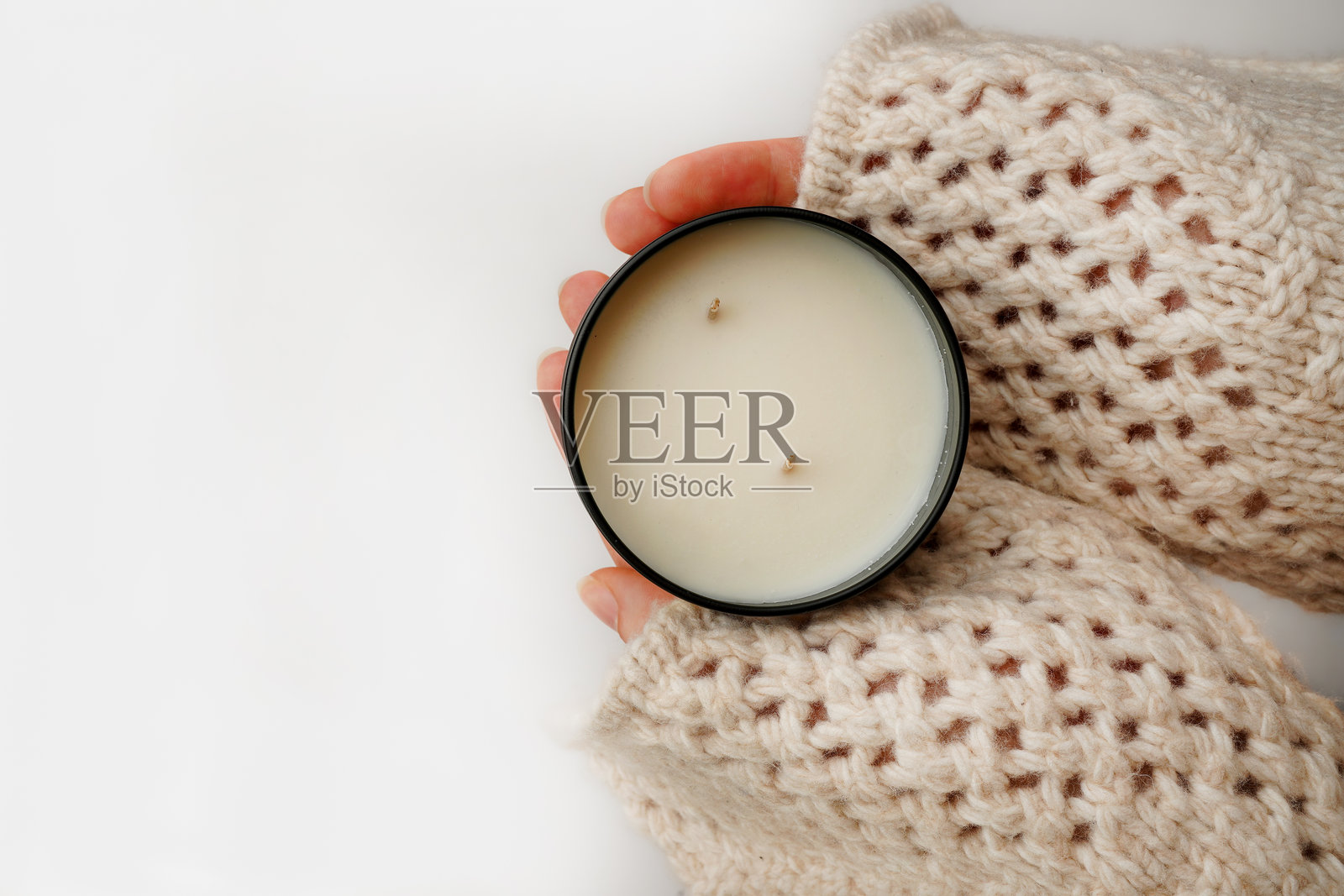 手中捧着蜡烛,穿着针织毛衣,背景为白色。温馨简约的美学,带来温暖与放松。照片摄影图片