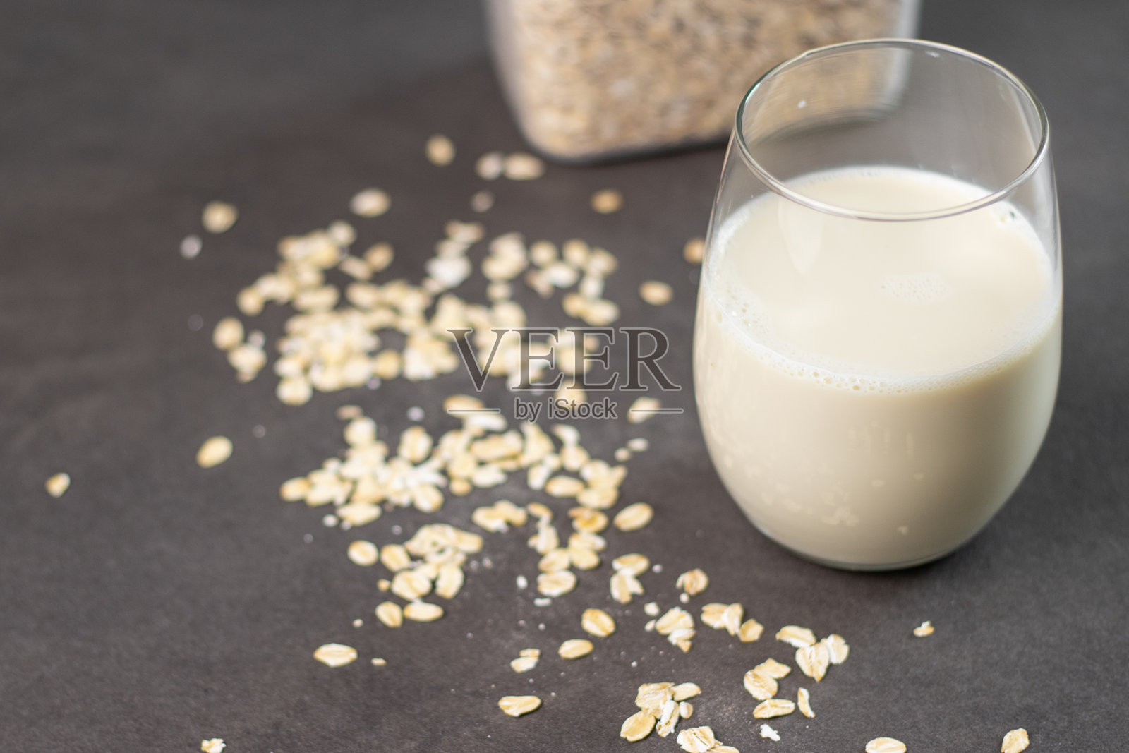 一杯无乳糖燕麦奶和一个装有燕麦的盒子放在厨房桌子上,背景模糊。植物性和非乳制替代奶概念照片摄影图片