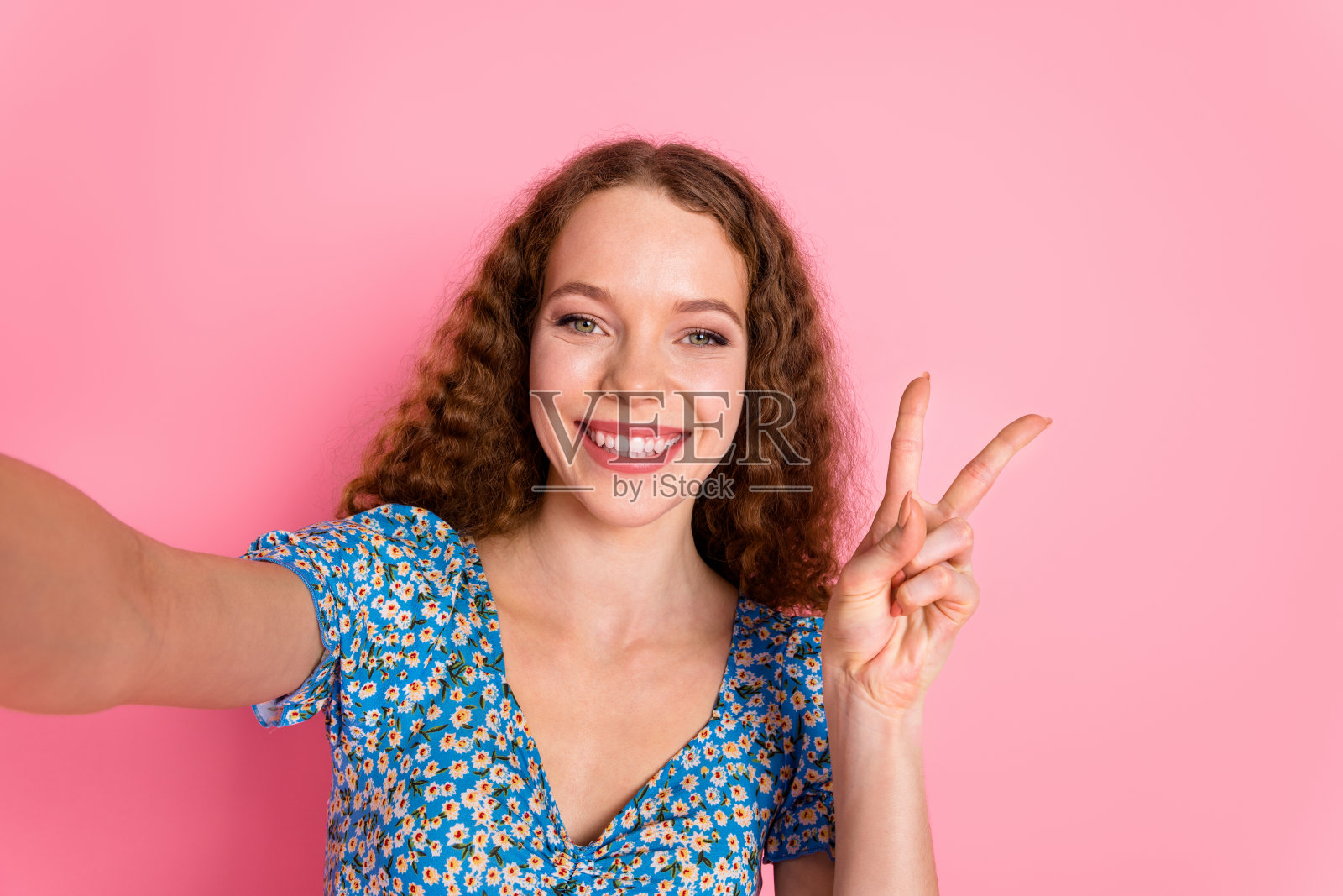 微笑的女性在粉色背景下拍自拍,做出和平手势照片摄影图片