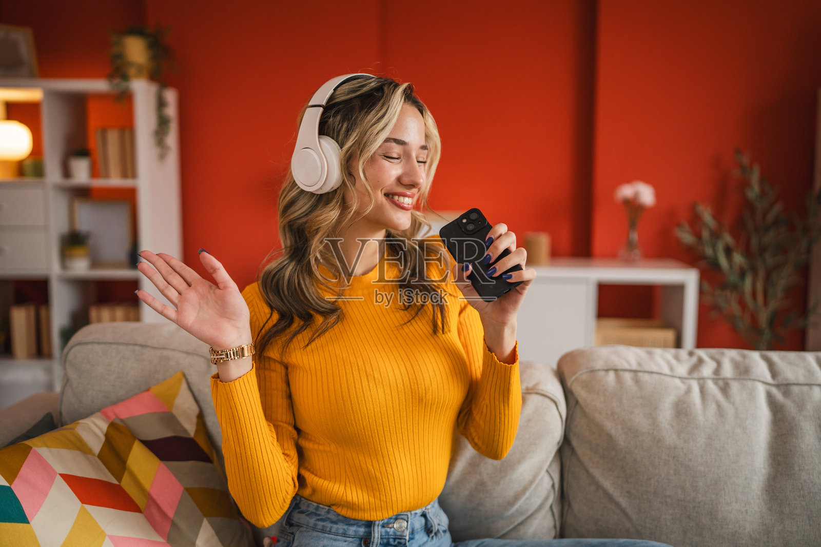 美丽的金发年轻女孩在手机上唱歌,戴着耳机。照片摄影图片