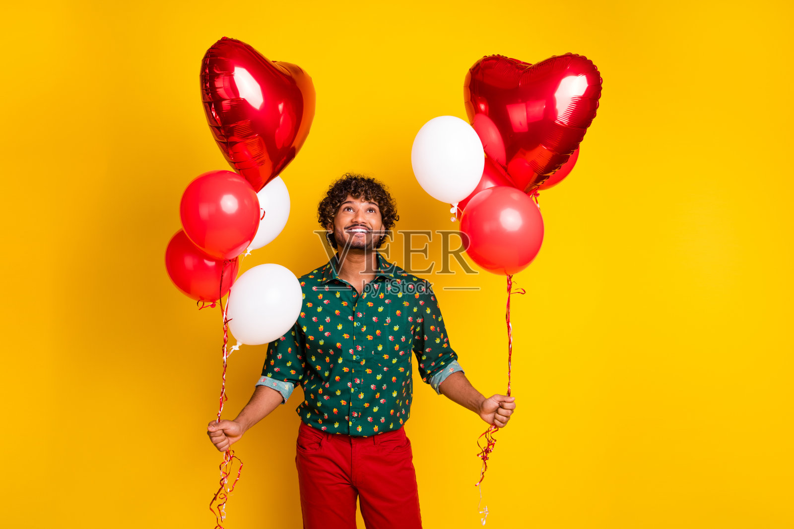 穿着时尚衣服的阳光帅气男士手持气球,背景为空旷的黄色。照片摄影图片