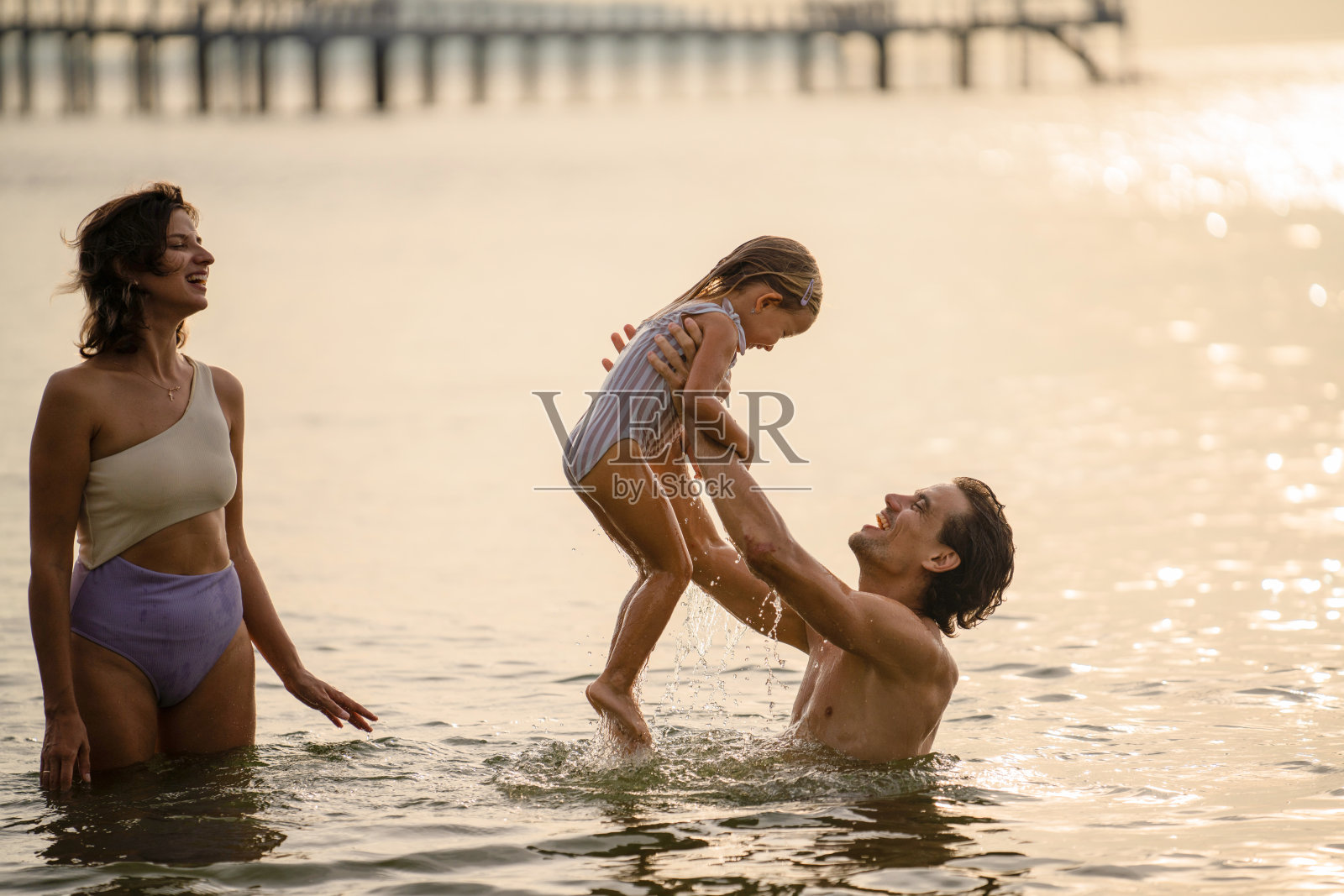 家庭在金色时光中享受水边宁静的时刻,伴随着光影倒影和轻柔的波浪。照片摄影图片