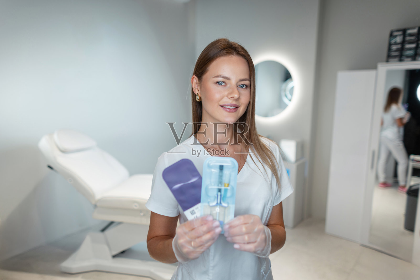 美丽的专业女医生穿着白大褂,在美容工作室中手持注射填充剂产品。美容与护肤。唇部增大,概念。选择医疗产品。照片摄影图片