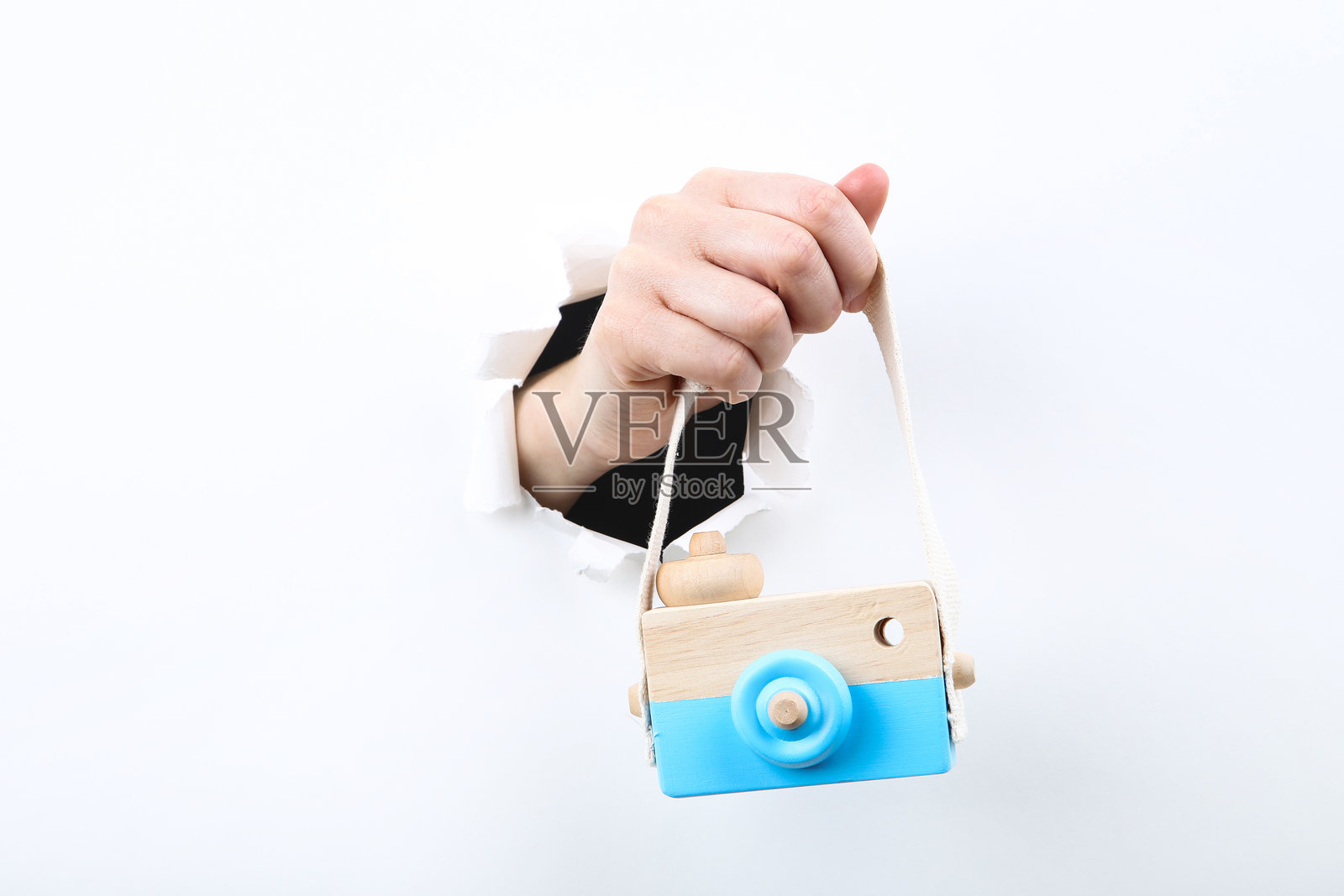 手握木制相机玩具从撕开的白纸中出现照片摄影图片