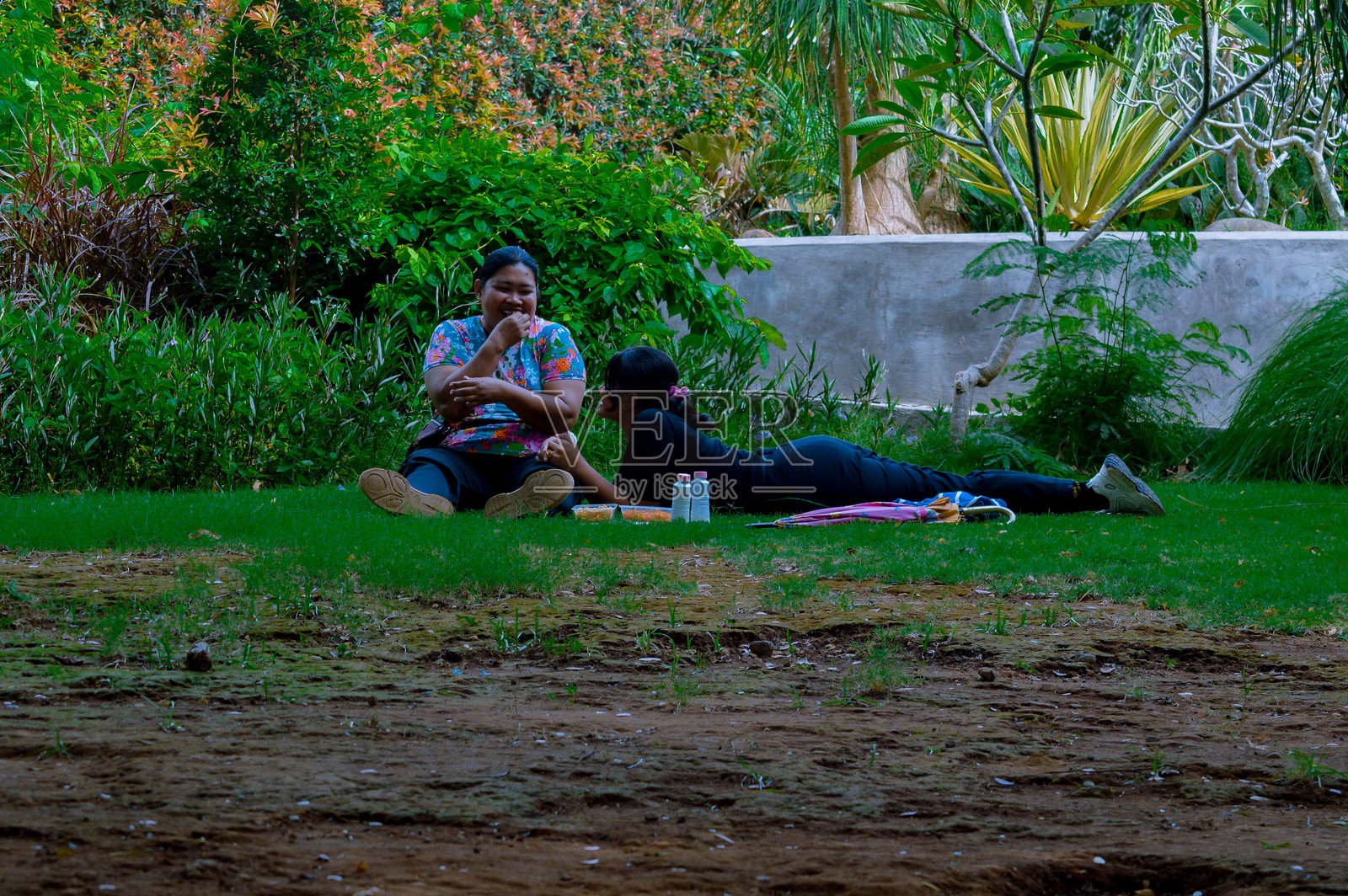 青少年躺在草地上,头朝下,旁边的女人在公园花园里吃零食照片摄影图片