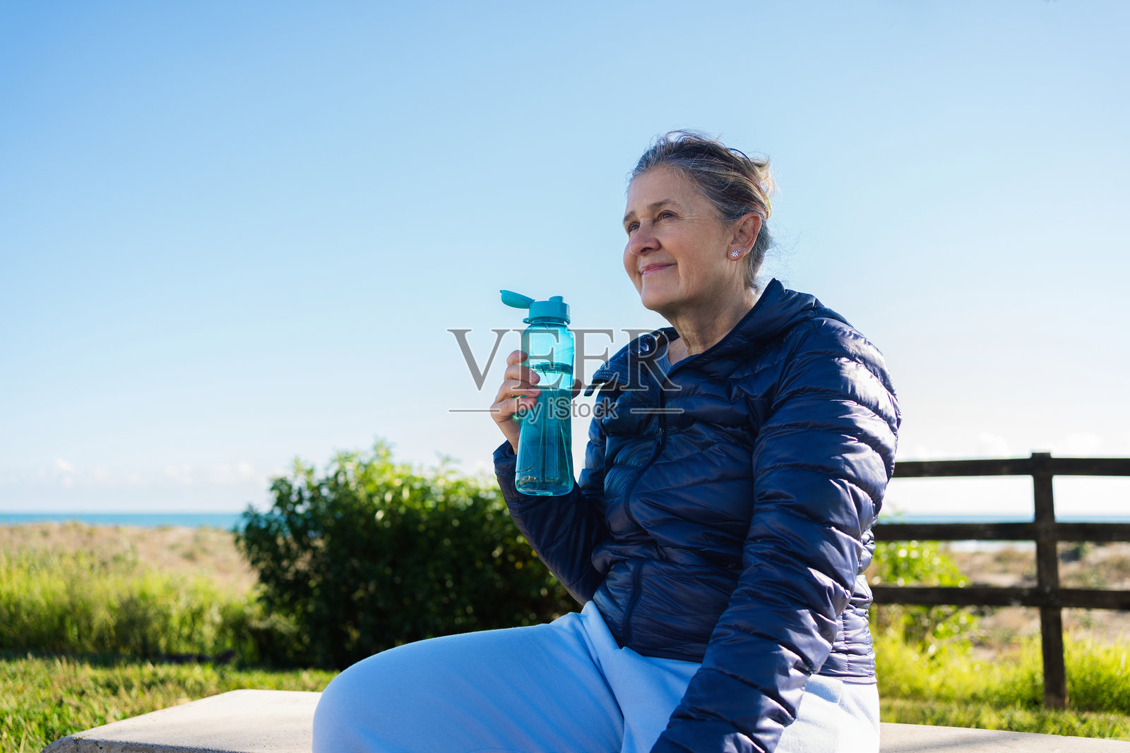 一位年长女性在户外锻炼后享受水分补给。照片摄影图片