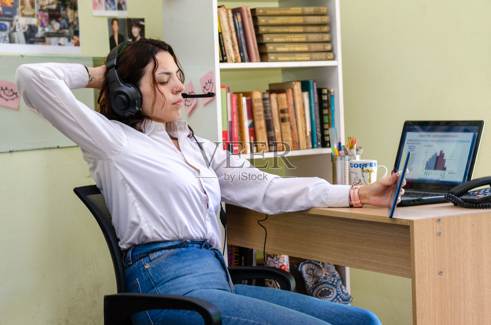 年轻女性认真地看着平板电脑,戴着耳机在家工作,旁边有笔记本电脑。照片摄影图片