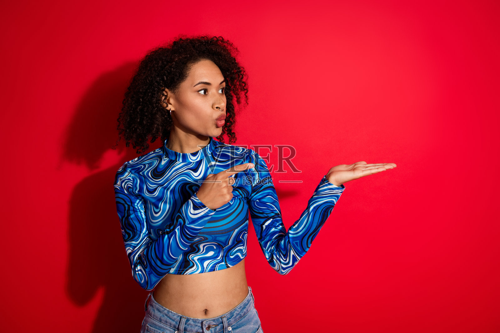 年轻时尚的女性在鲜艳的红色背景前指着并用手势表达。照片摄影图片