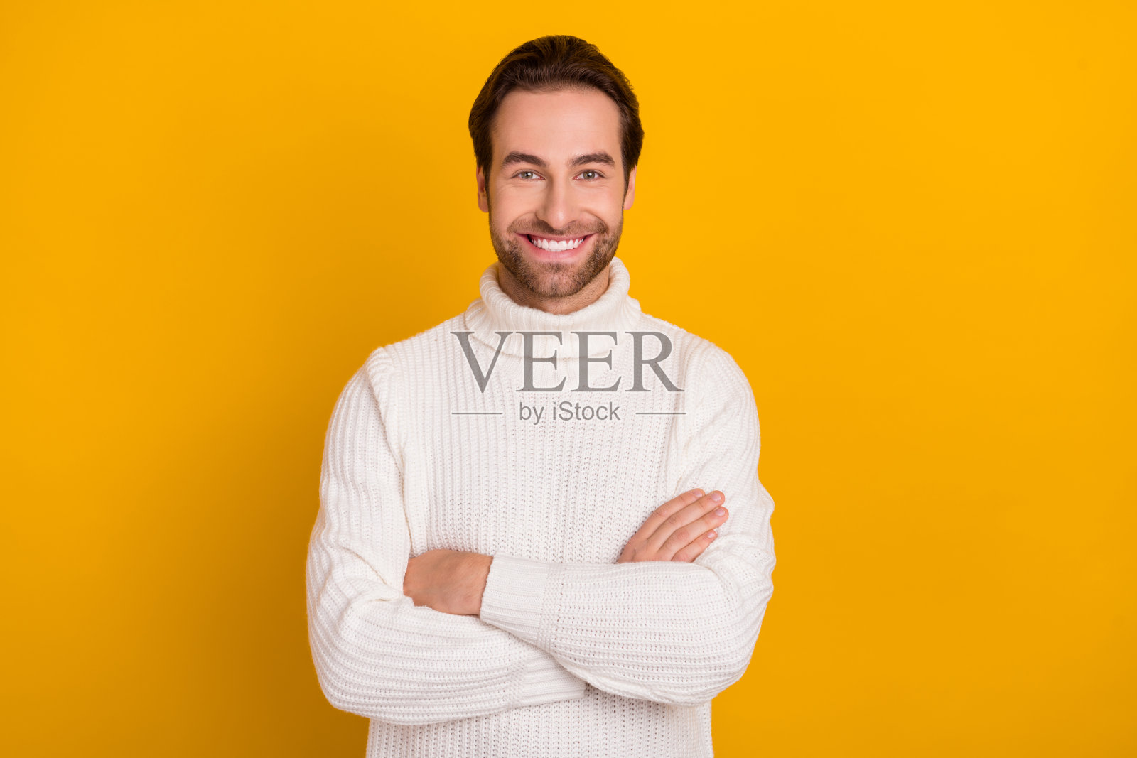 自信开朗的男士双臂交叉,面带灿烂笑容,穿着白色毛衣,背景为黄色。照片摄影图片