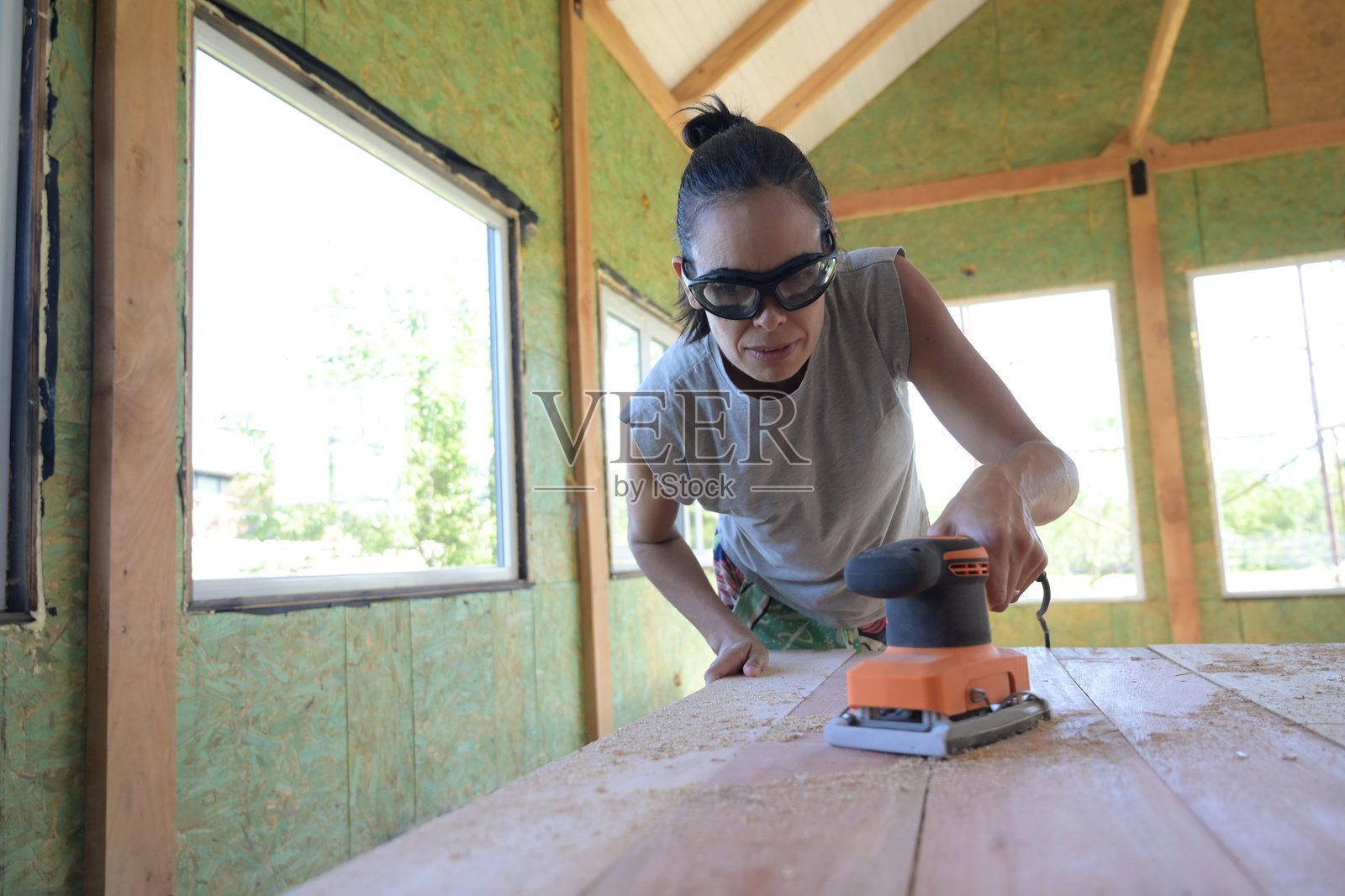 女性在木材上使用圆盘砂光机。照片摄影图片