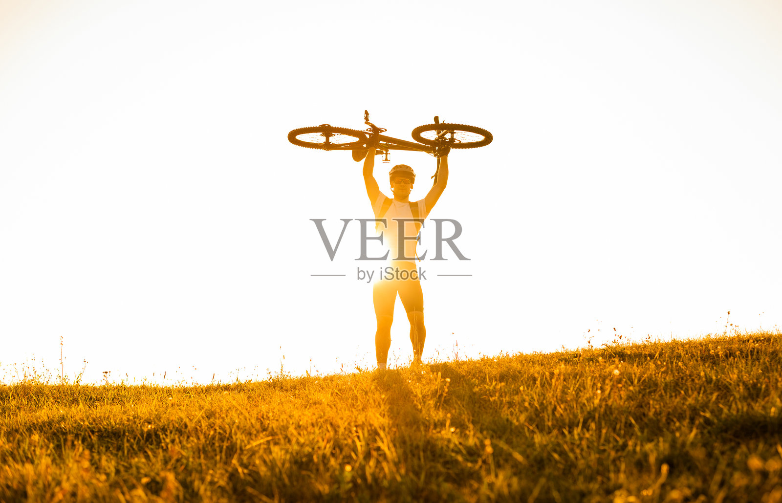 快乐的骑自行车男子在阳光背景下庆祝胜利,举起自行车,象征着体育成功的胜利。照片摄影图片