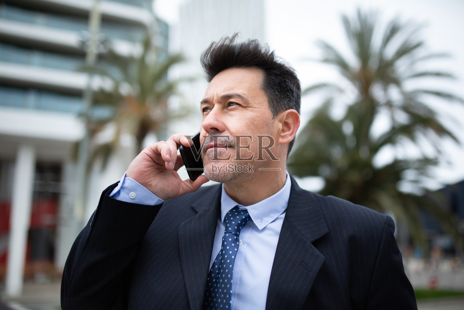 成熟的商人在城市外面站着并在打手机。照片摄影图片