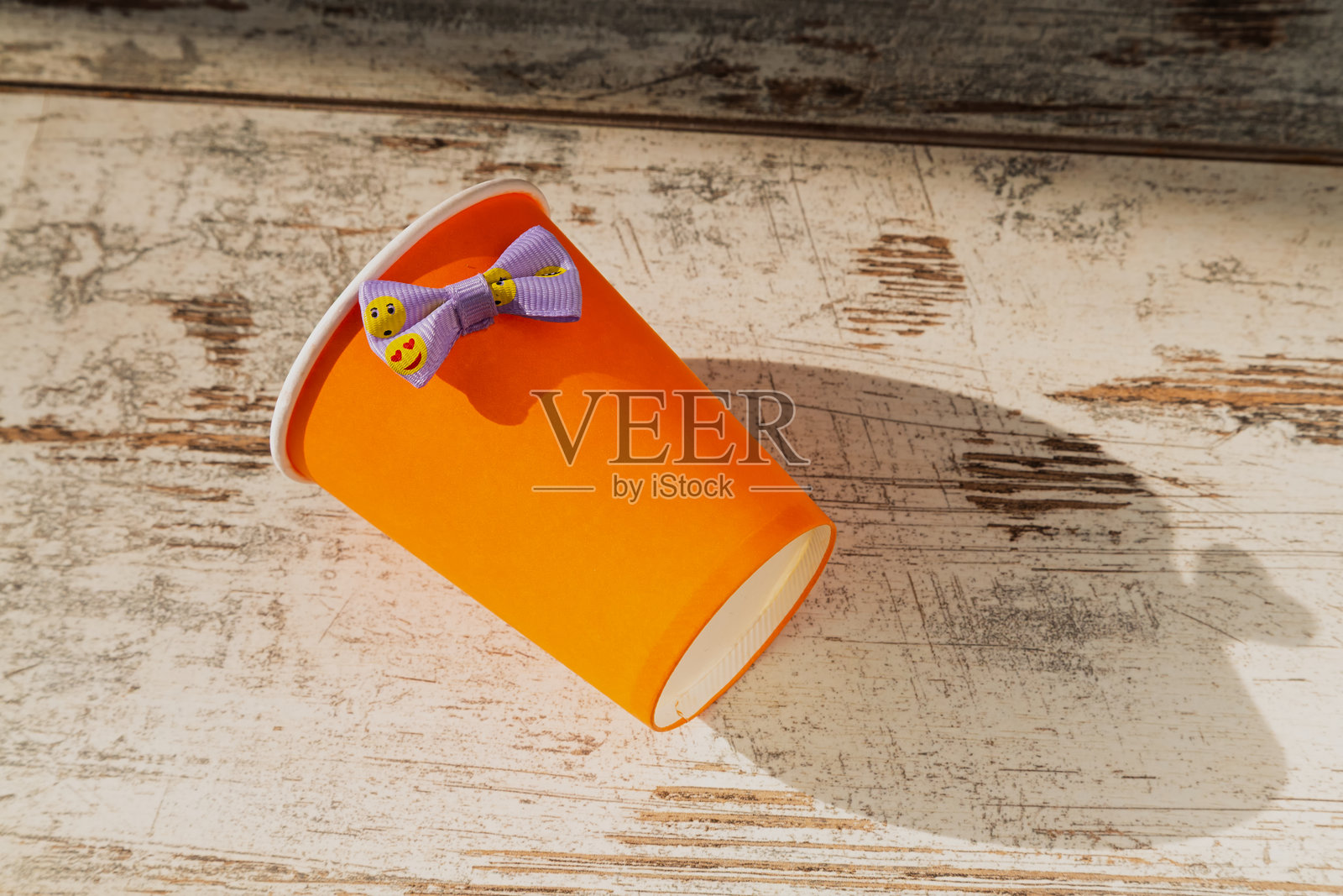 阳光下桌子上的纸橙色一次性杯子上系着一条欢快的丝带。庆祝的轻松氛围、企业的节日气息,以及派对的准备。照片摄影图片