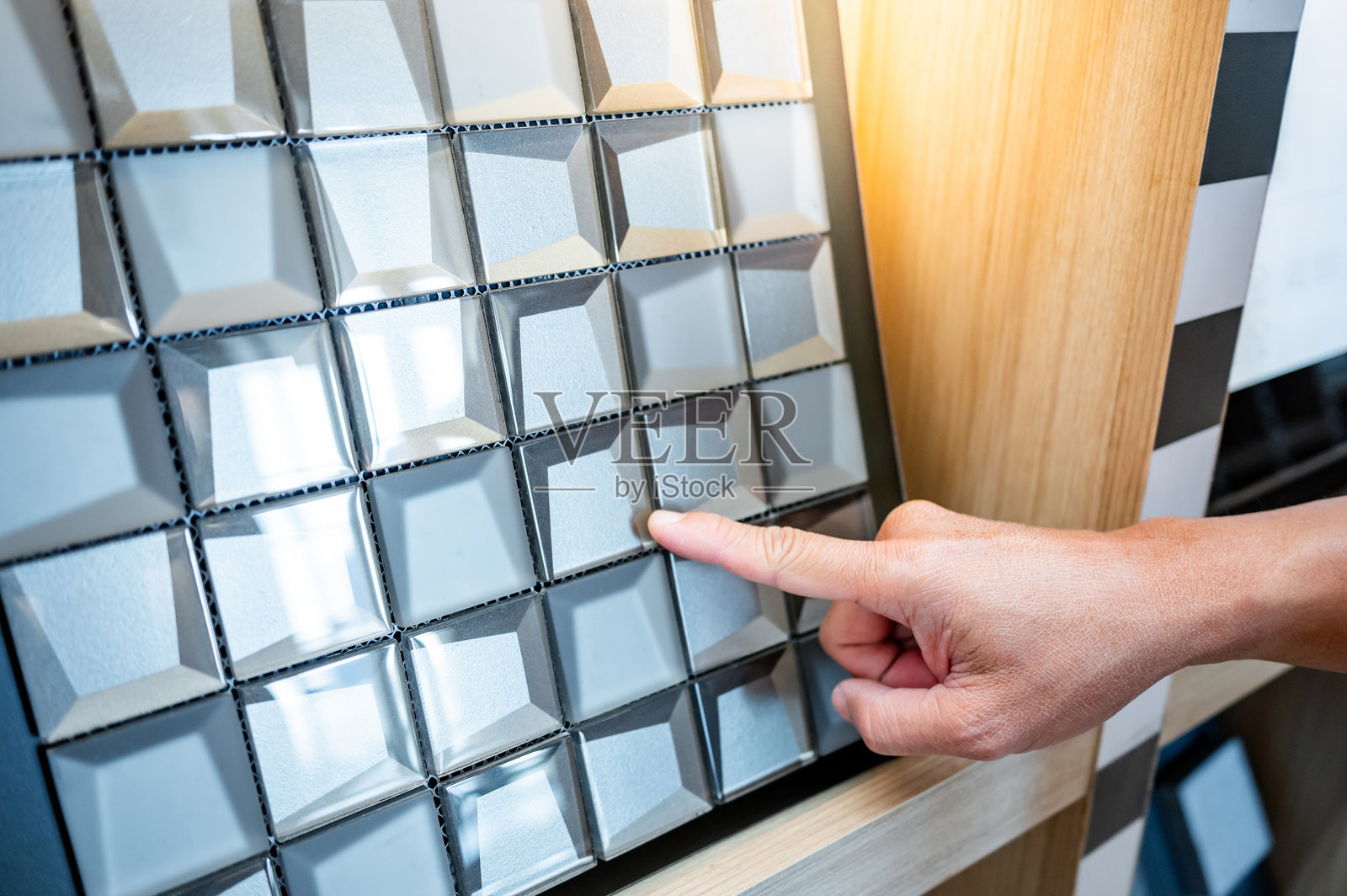 设计师的手指向材料展厅中陶瓷系列展示架上的金属马赛克瓷砖图案。为浴室装饰选择墙面饰面。照片摄影图片