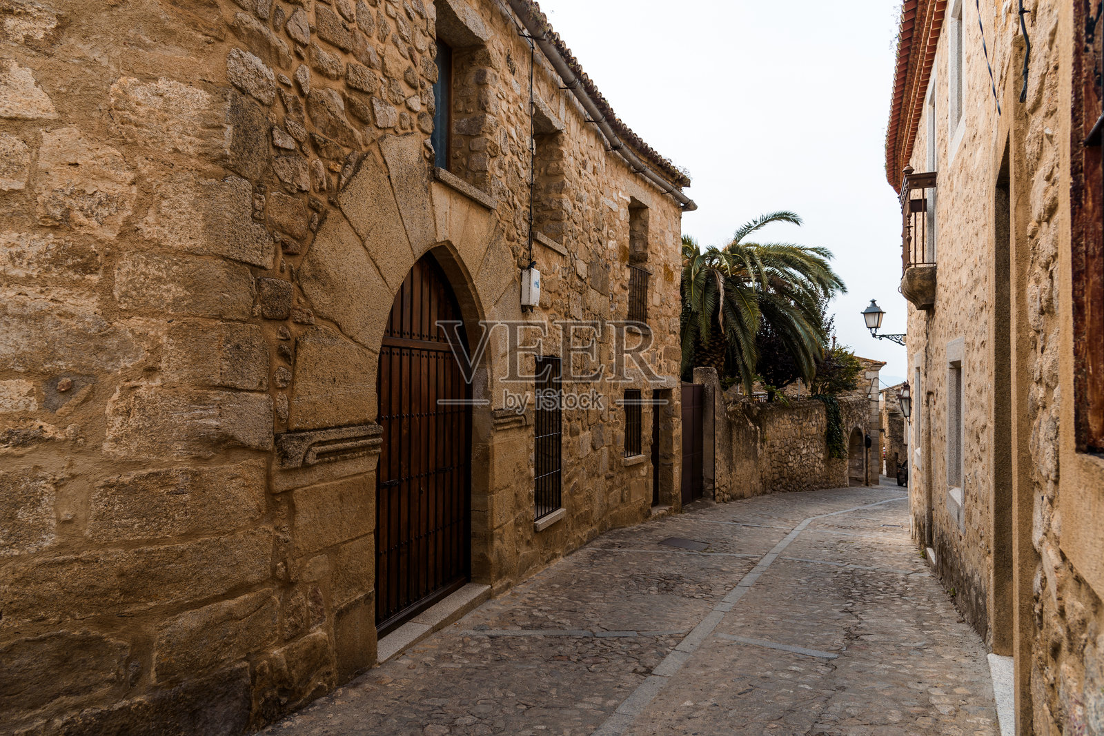 探索西班牙特鲁希略一条蜿蜒的鹅卵石街道,周围是历史悠久的石建筑。照片摄影图片