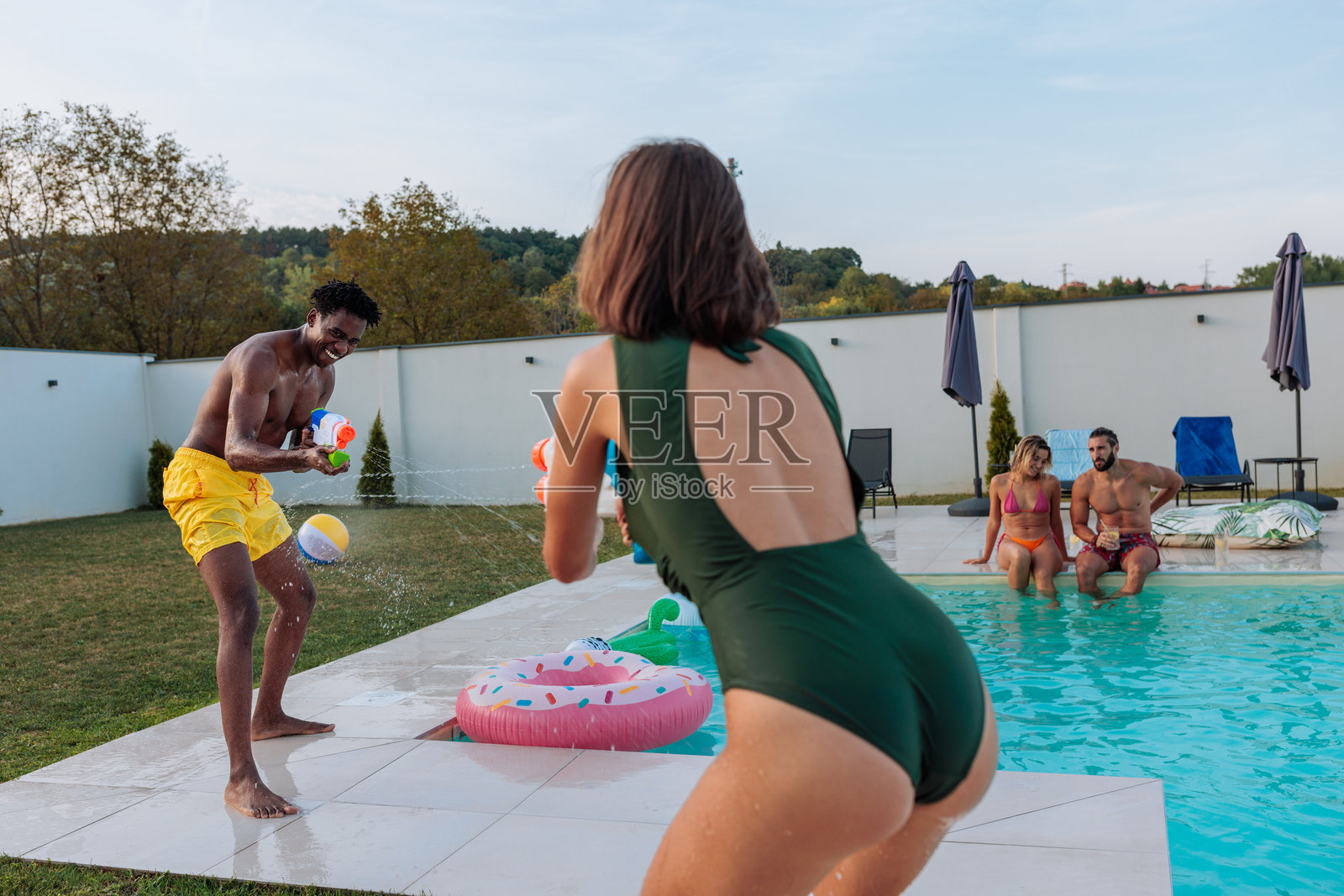 朋友们在夏季假期时在泳池边玩水枪照片摄影图片